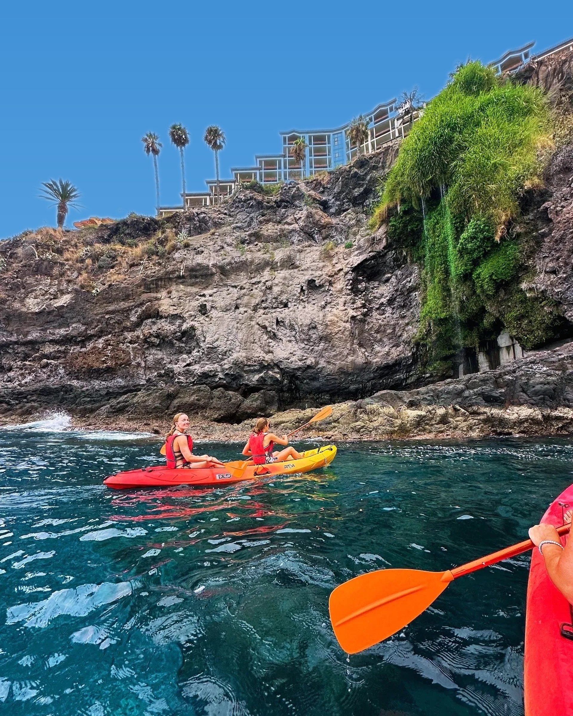 Group of kayakers on red and yellow kayaks in front of a lush green cliff near Funchal, Madeira