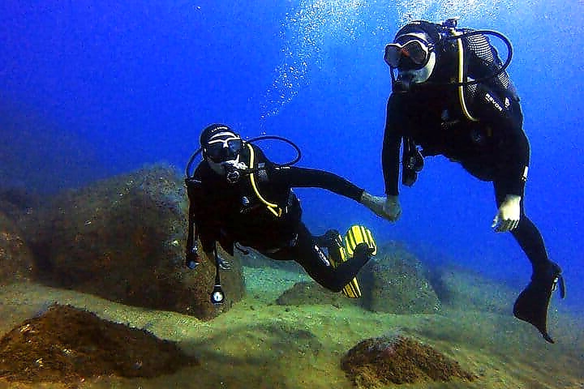 Two scuba divers exploring the underwater rocky seabed during an ocean dive in Funchal, Madeira