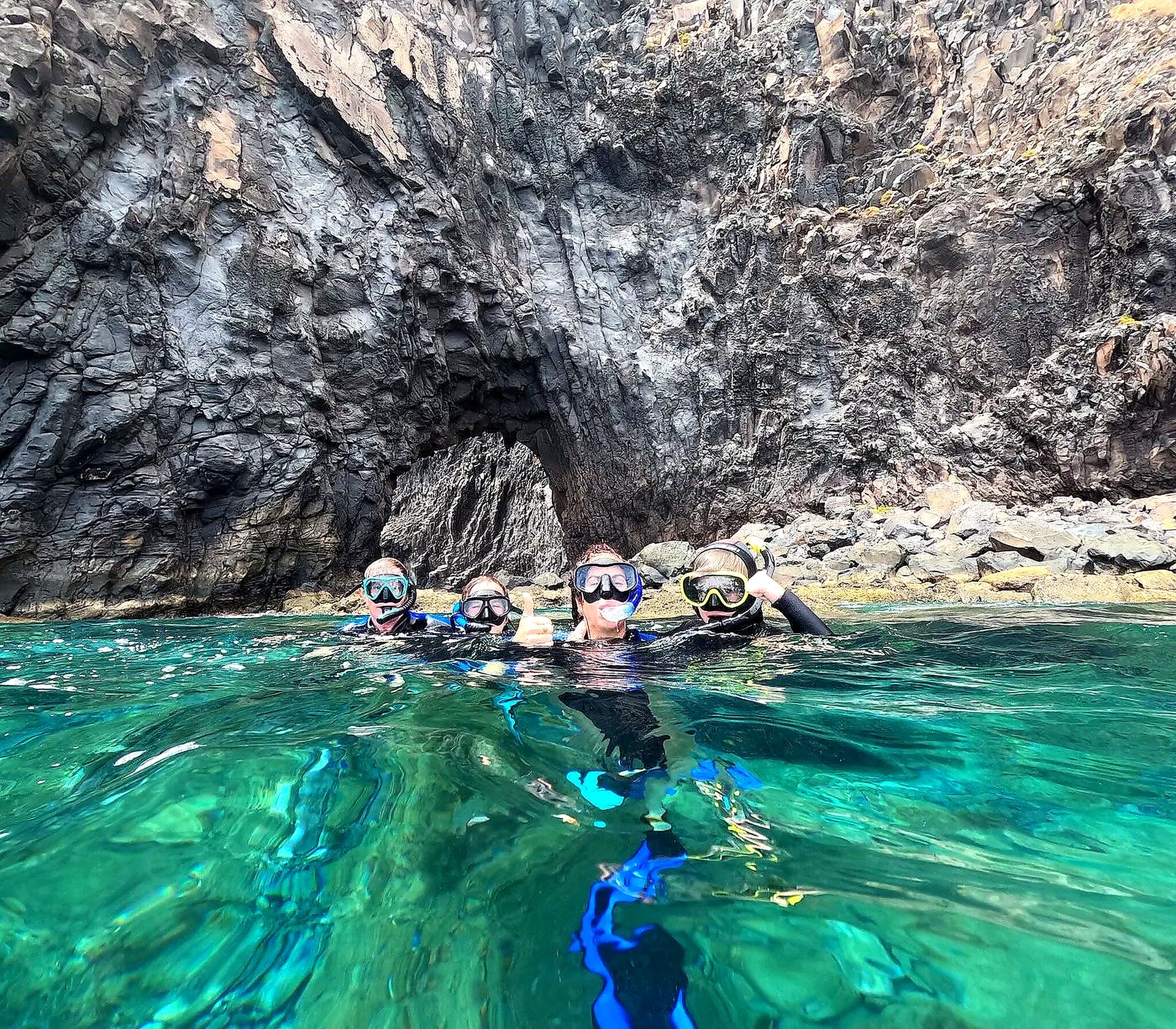 Group of snorkelers in green water in front of a volcanic rock arch at Ponta de São Lourenço, Madeira