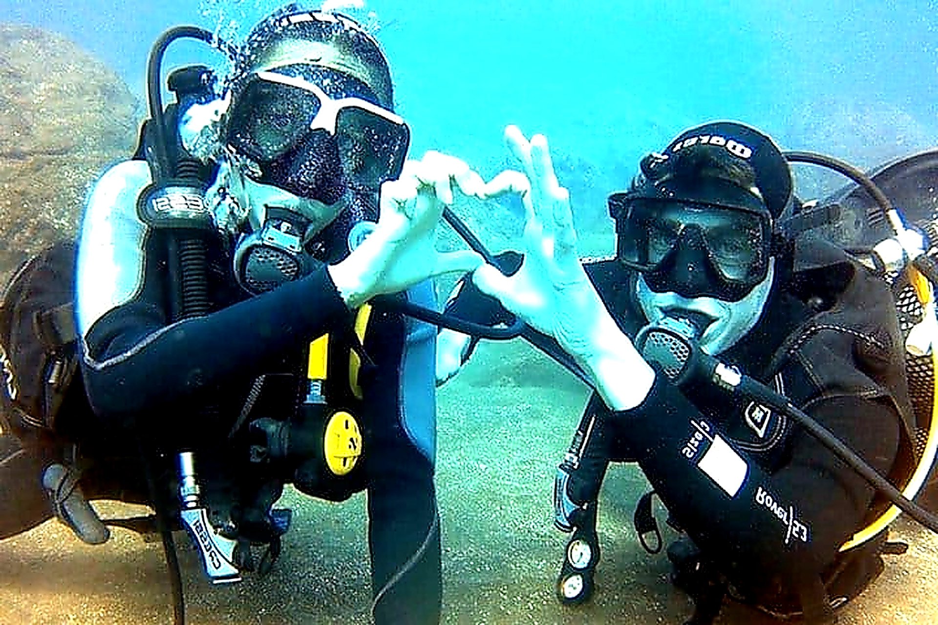 Two happy scuba divers making a heart shape with their hands underwater in Funchal, Madeira