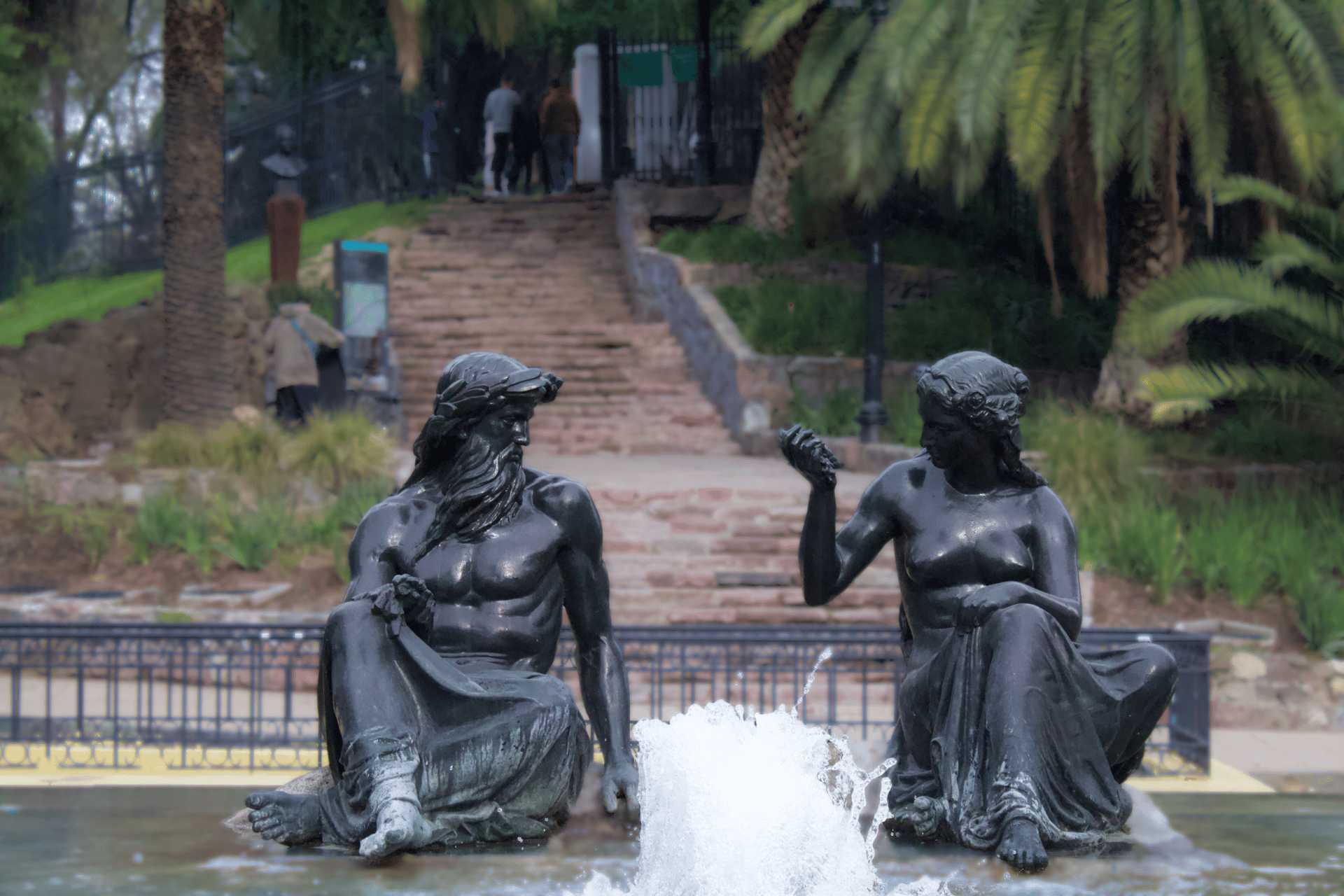 2 person walking on pathway between green trees during daytime