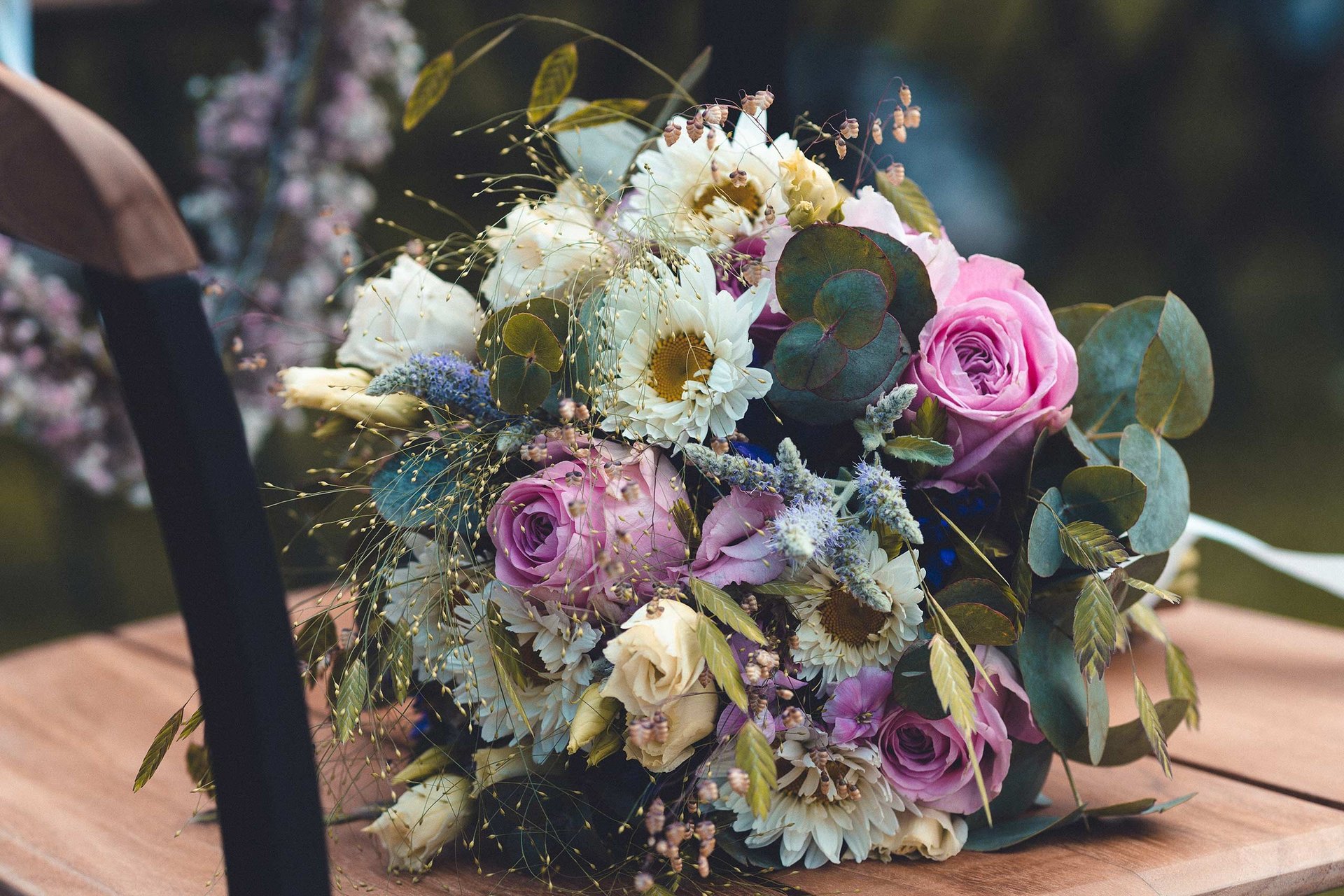 Bunter Brautstrauß mit Rosen und Eukalyptus auf einem Holzstuhl. Hochzeitsfloristik-Foto: Just Perspectives.
