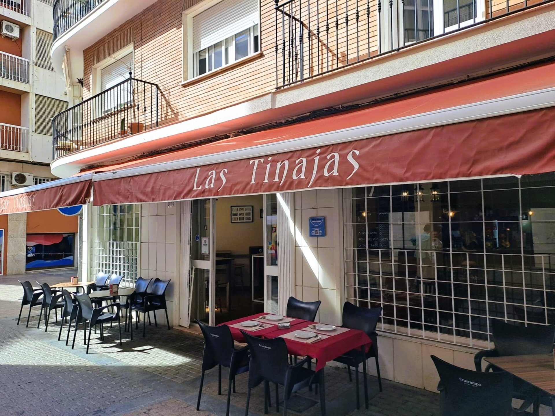 Historia del Bar Las Tinajas Huelva reflejada en su fachada exterior y terraza, con mesas listas para recibir a los clientes.