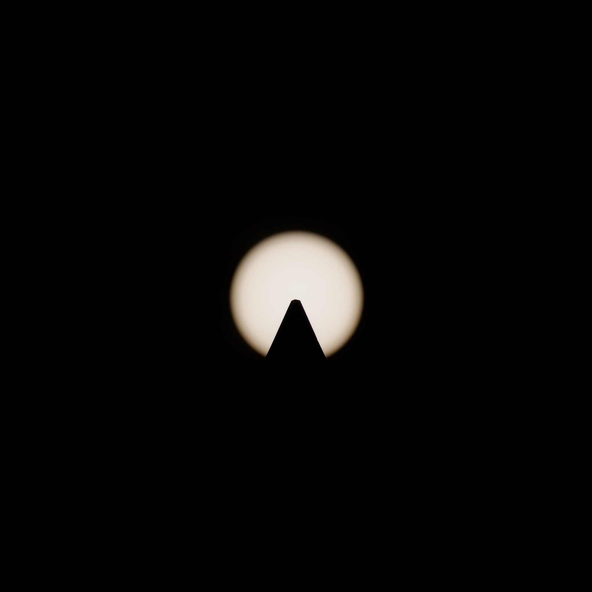 Symmetrical silhouette of an obelisk peak centered against a glowing sun, captured with a solar filter.