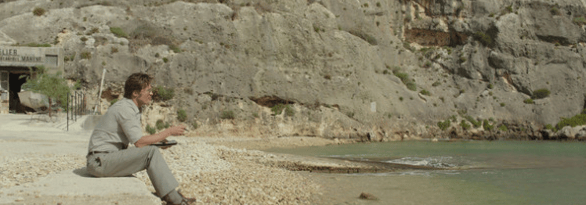 Brad Pitt sits on a beach in the movie By the Sea.