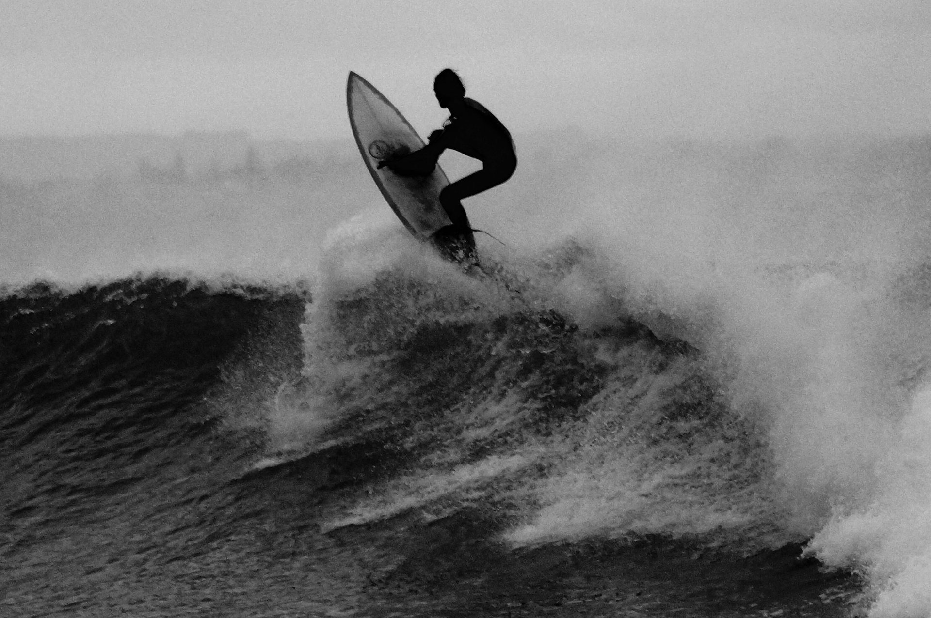 greyscale photography of person carrying surfboard on seashore