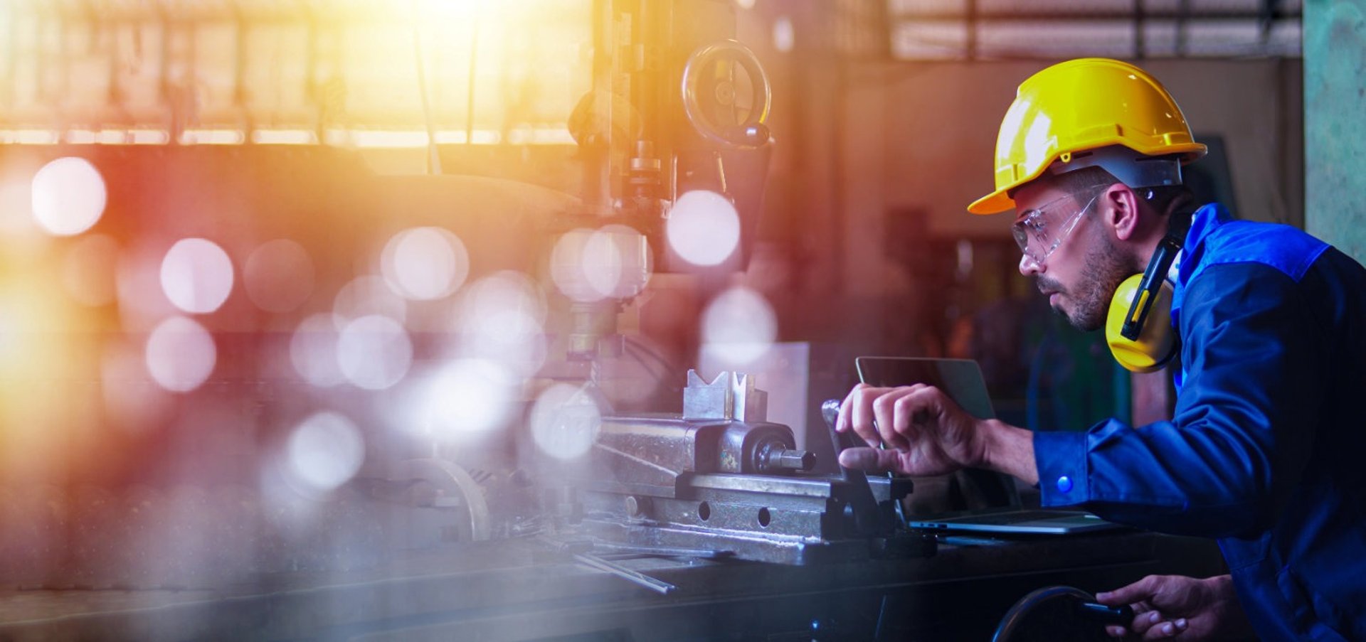 A man in a blue coveral and yellow helmet is welding metal