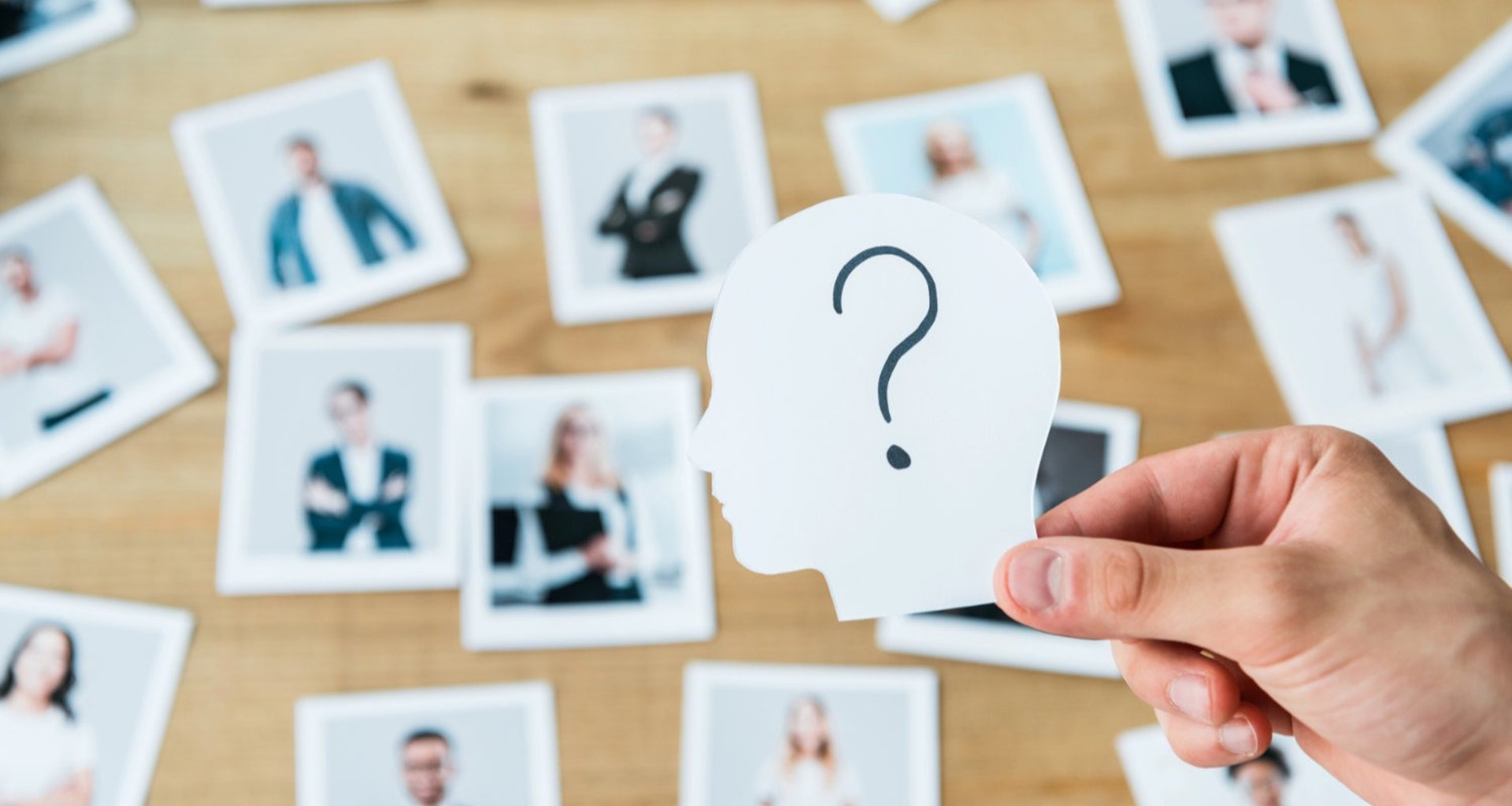 A hand holds a unidentified white paper head above a table with diffuse photos