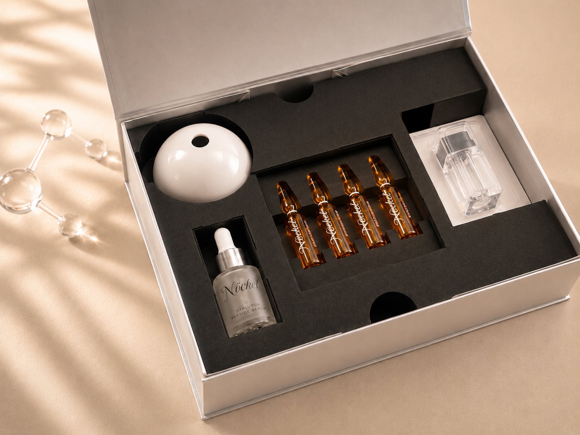 Luxuriöses NÖCKELKosmetik-Set mit Serum, Schutzcreme und Applikator in eleganter Box auf neutralem Hintergrund.