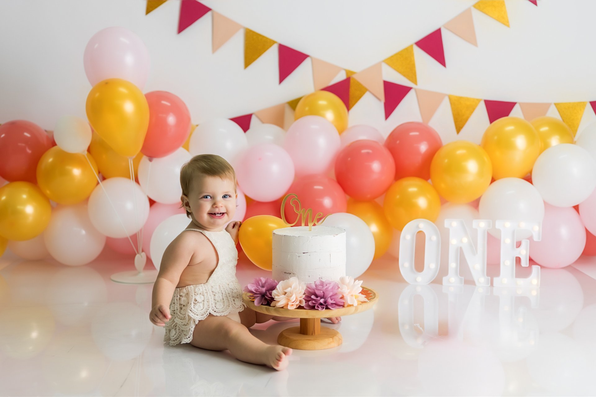 bebé sentada junto a tarta delante de globos en la sesión de smash cake