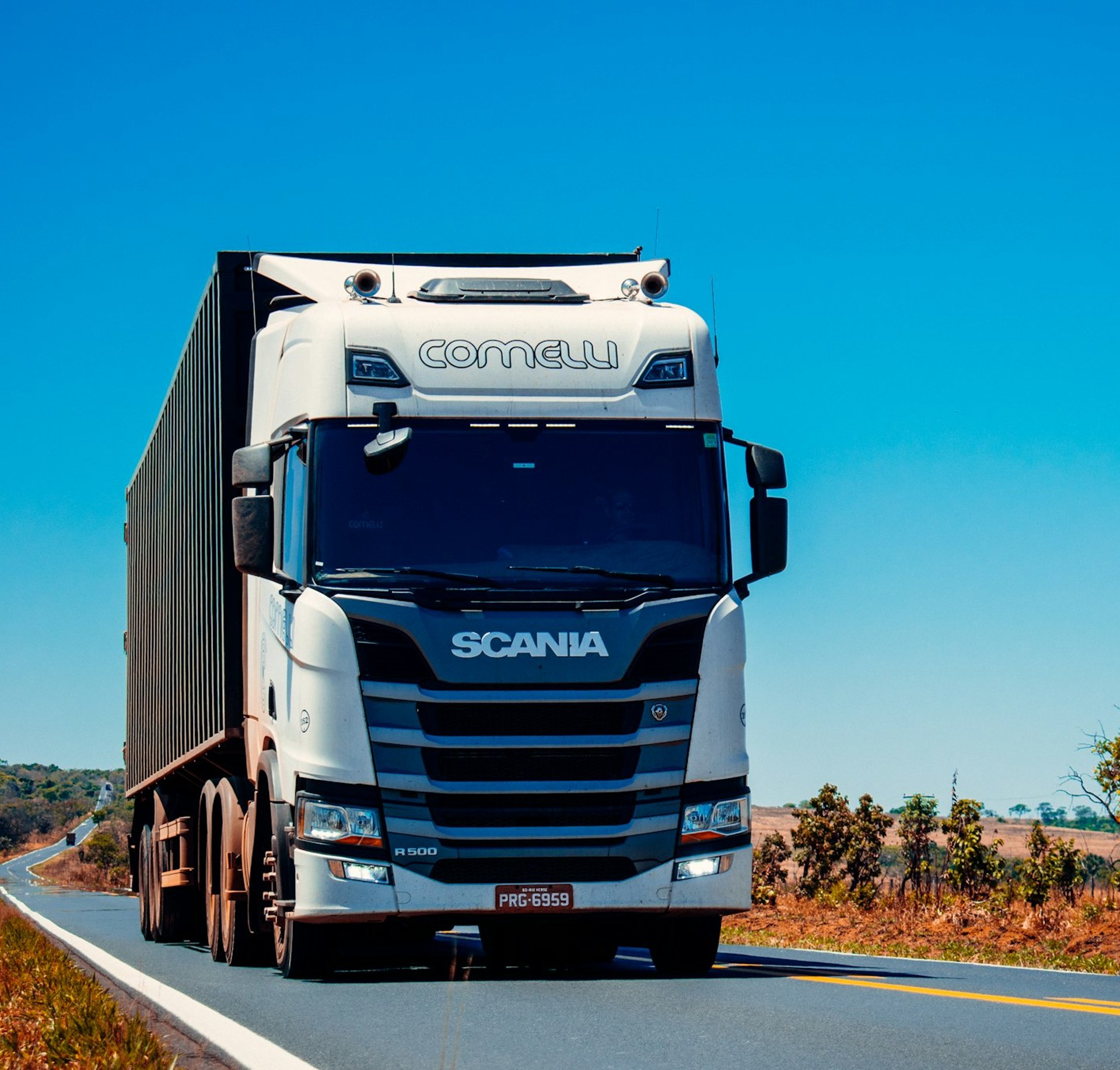 a white truck driving down a road next to a lush green field