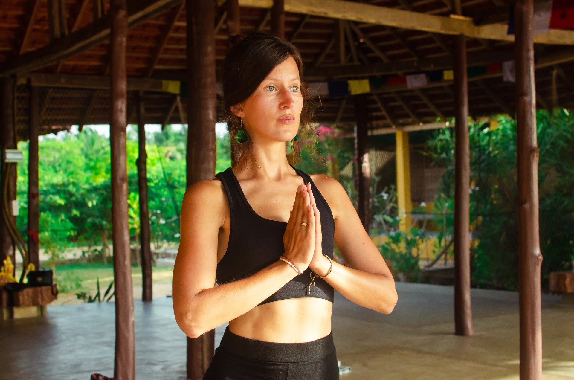 Yogateacher Isabel Maass in Namaste mudra before lush green, introducing Everyday Essentials mindfulness tools.