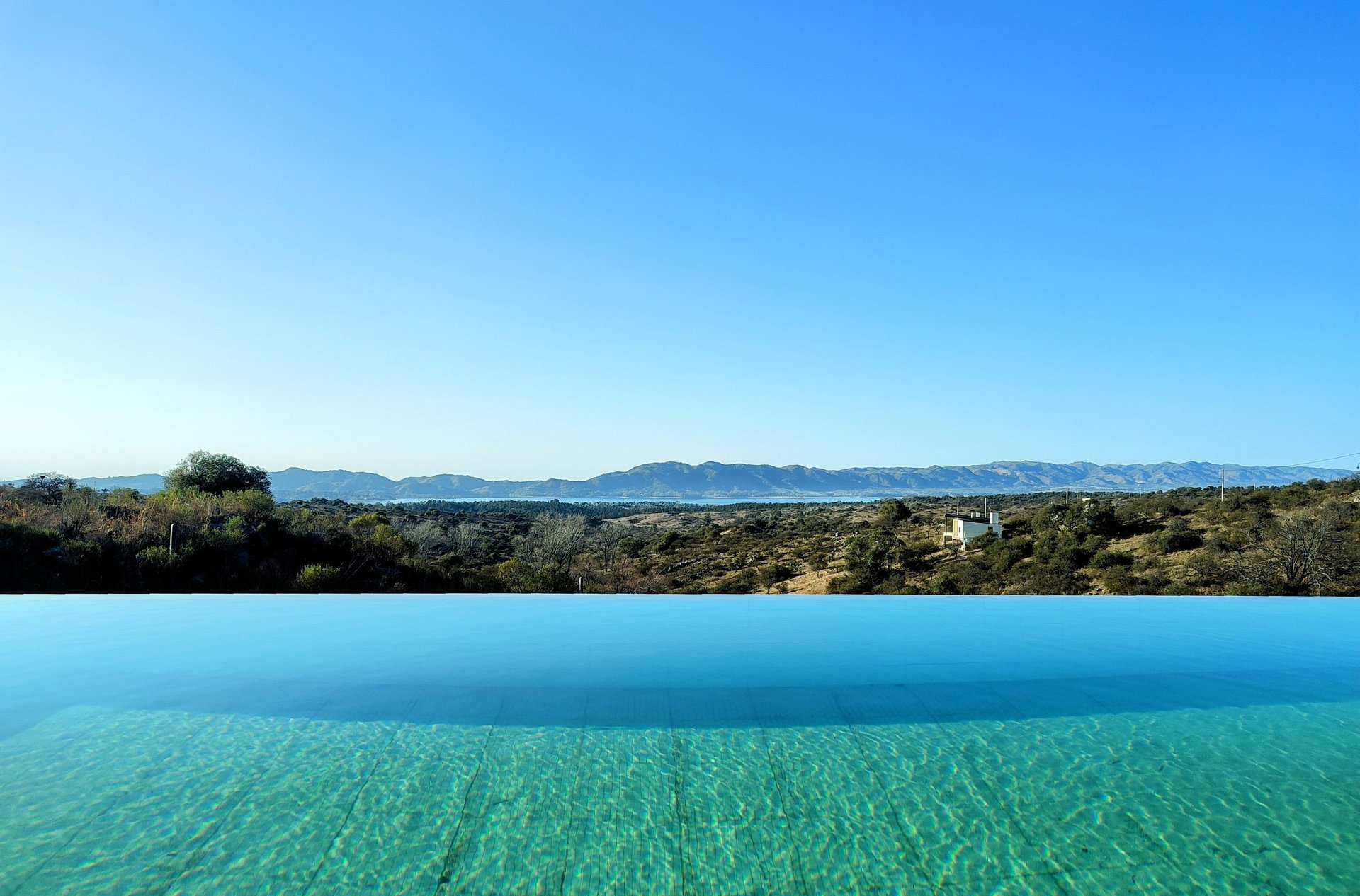 Foto de Pileta con borde infinito y de fondo el espectacular paisaje del dique los molinos y sierras en Córdoba. Casa Puente