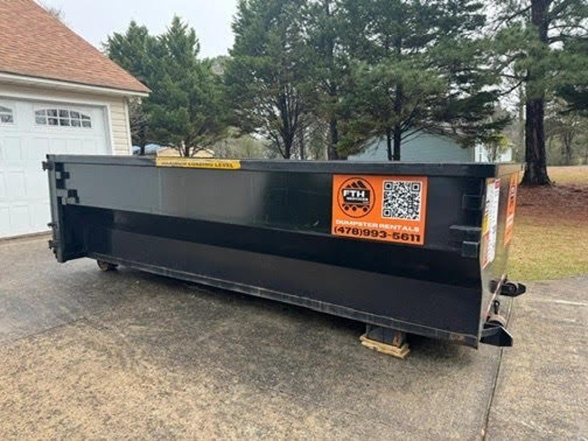 A black dumpster provided by FTH Services. The dumpster is set up on a residential driveway.