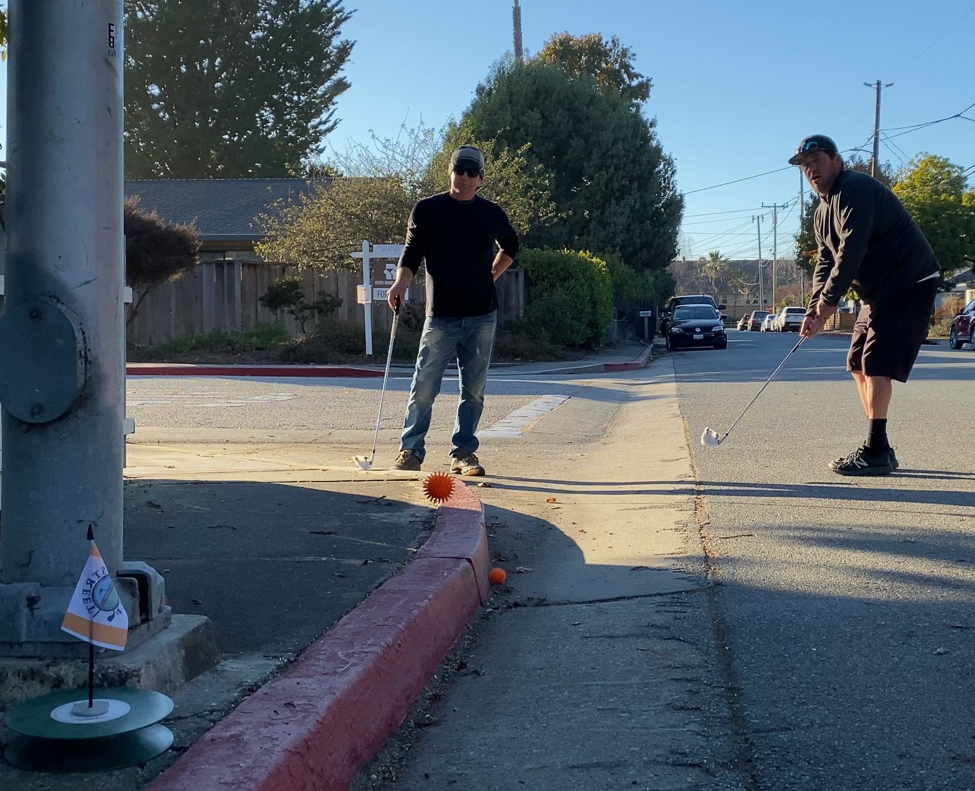 Street golf chip shot: two men aim for the urban capture hole