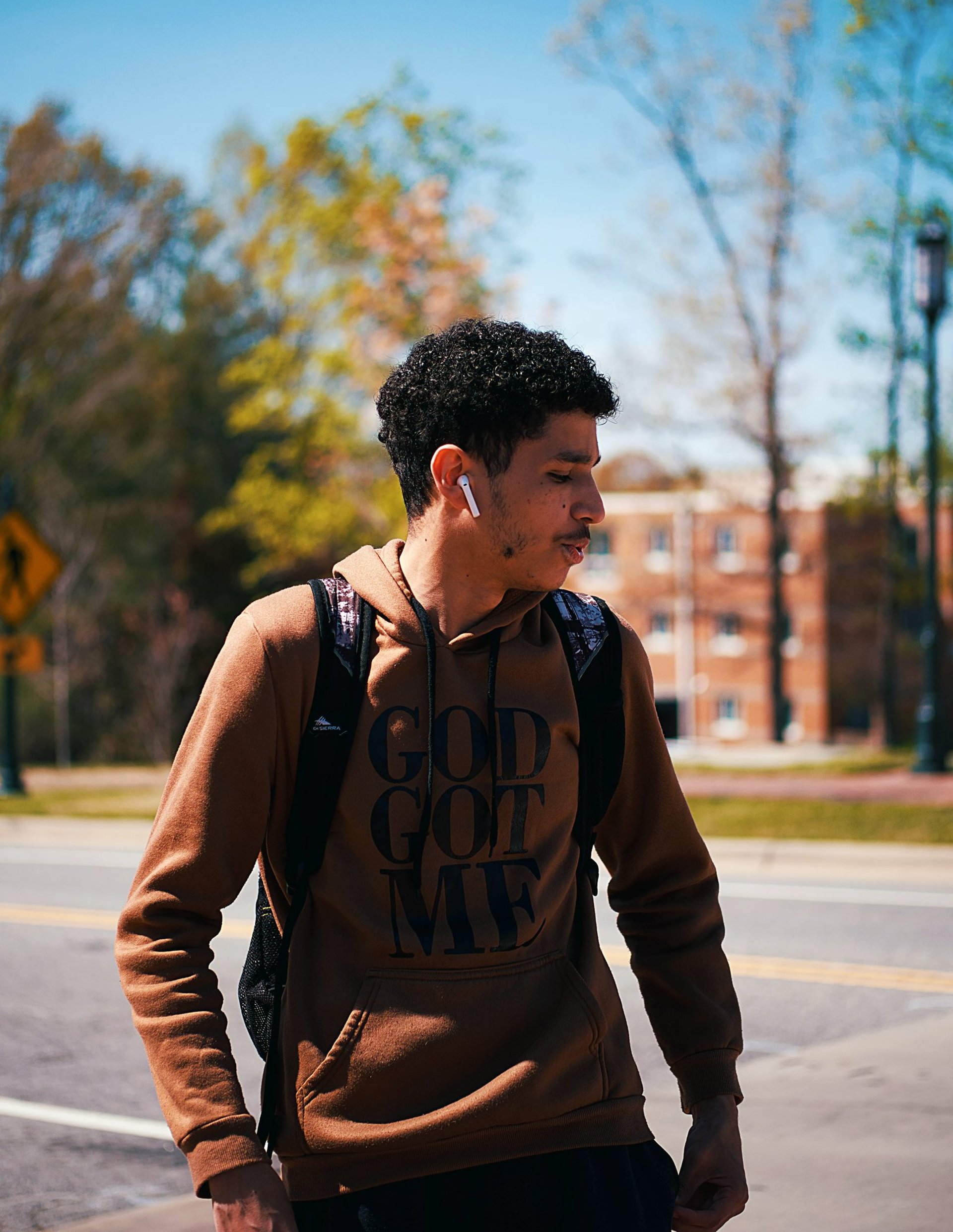 Young male college student looking to the side wearing a "God Got Me" hoodie while wearing Air Pods at UNC Charlotte campus.