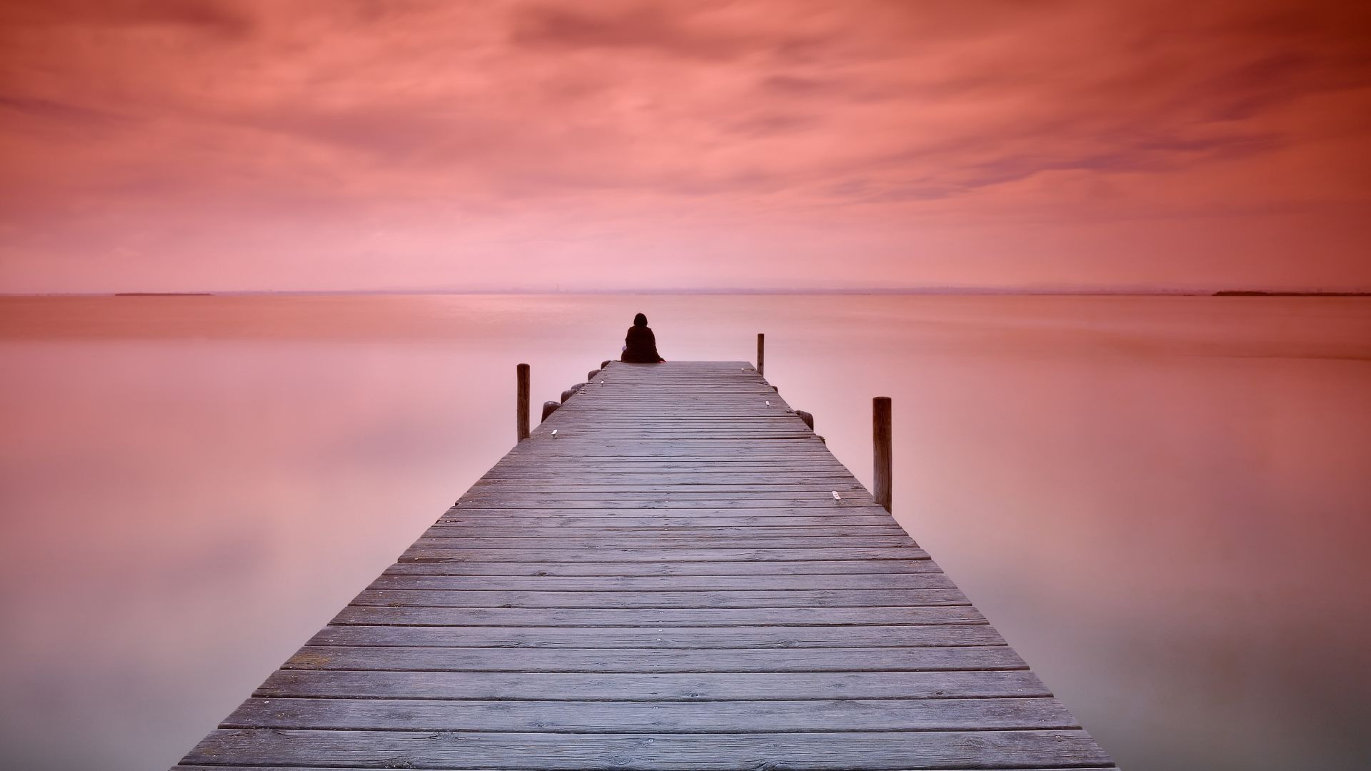 a minimist photograph of a person sitting at the end of a wooden jetty with a sunset sky for art photography