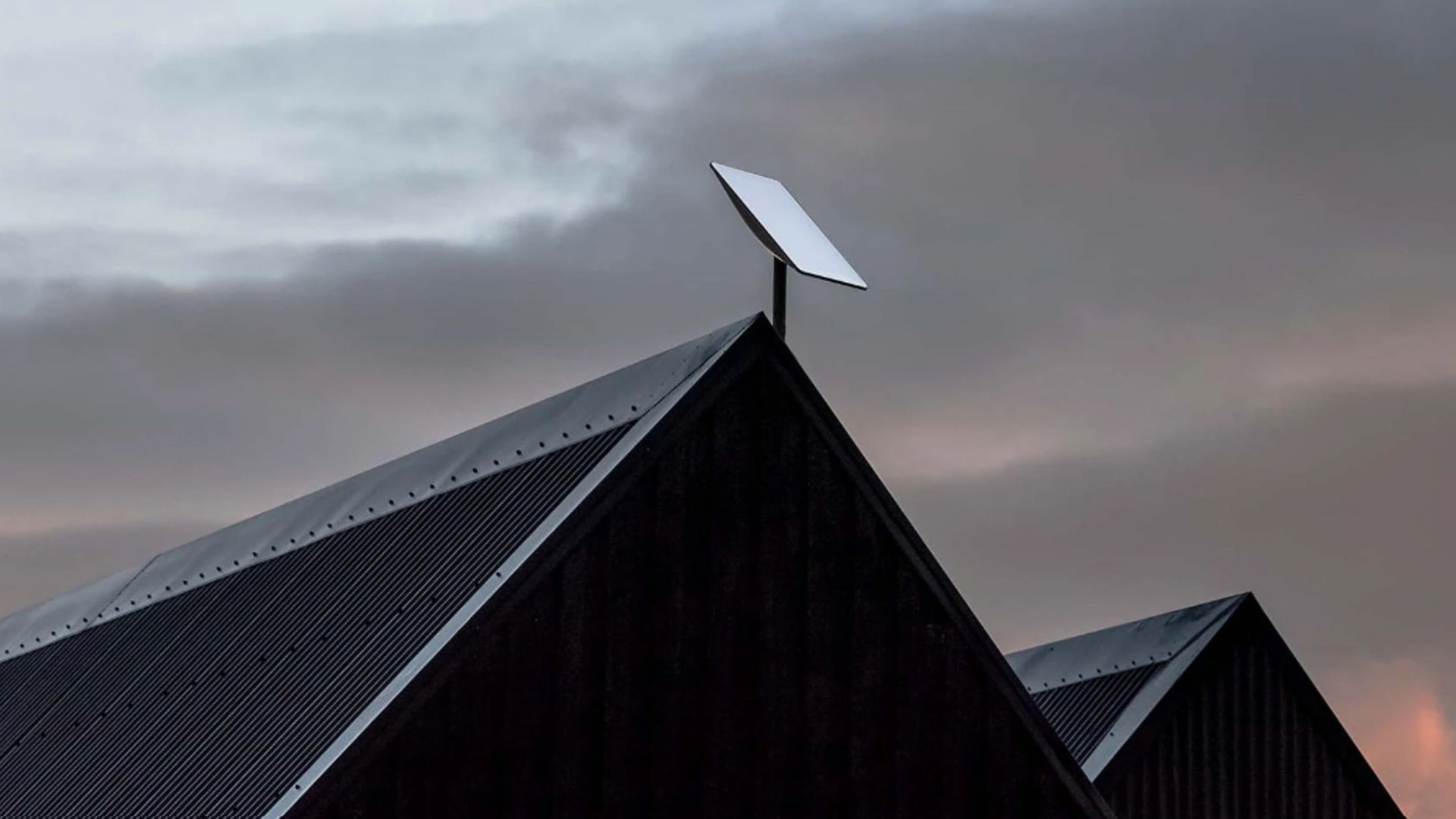 Starlink dish mounted on eave of house with blue sky in background