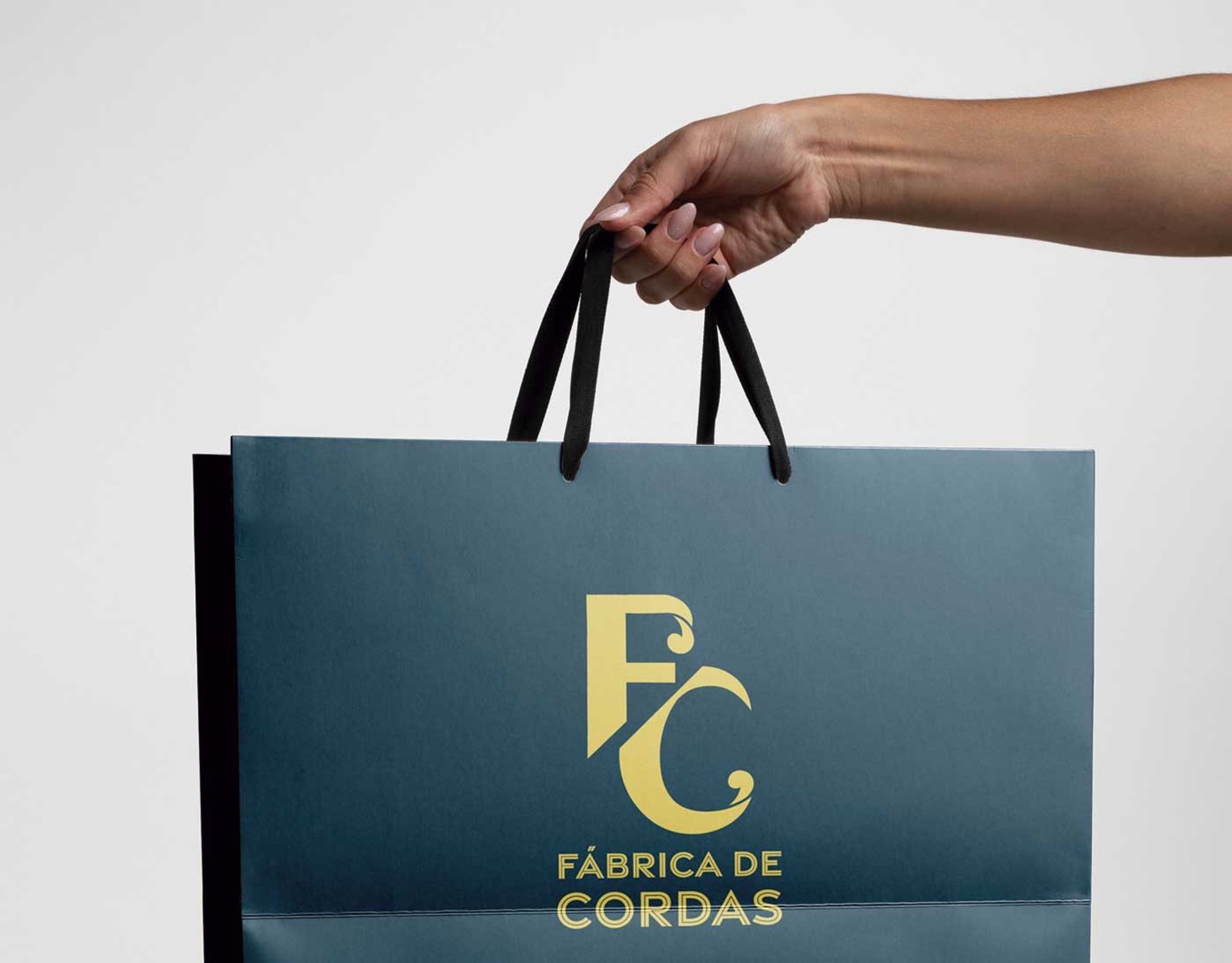 Mão segurando uma sacola com o logotipo da FC Fábrica de Cordas estampado, simbolizando compras e qualidade.