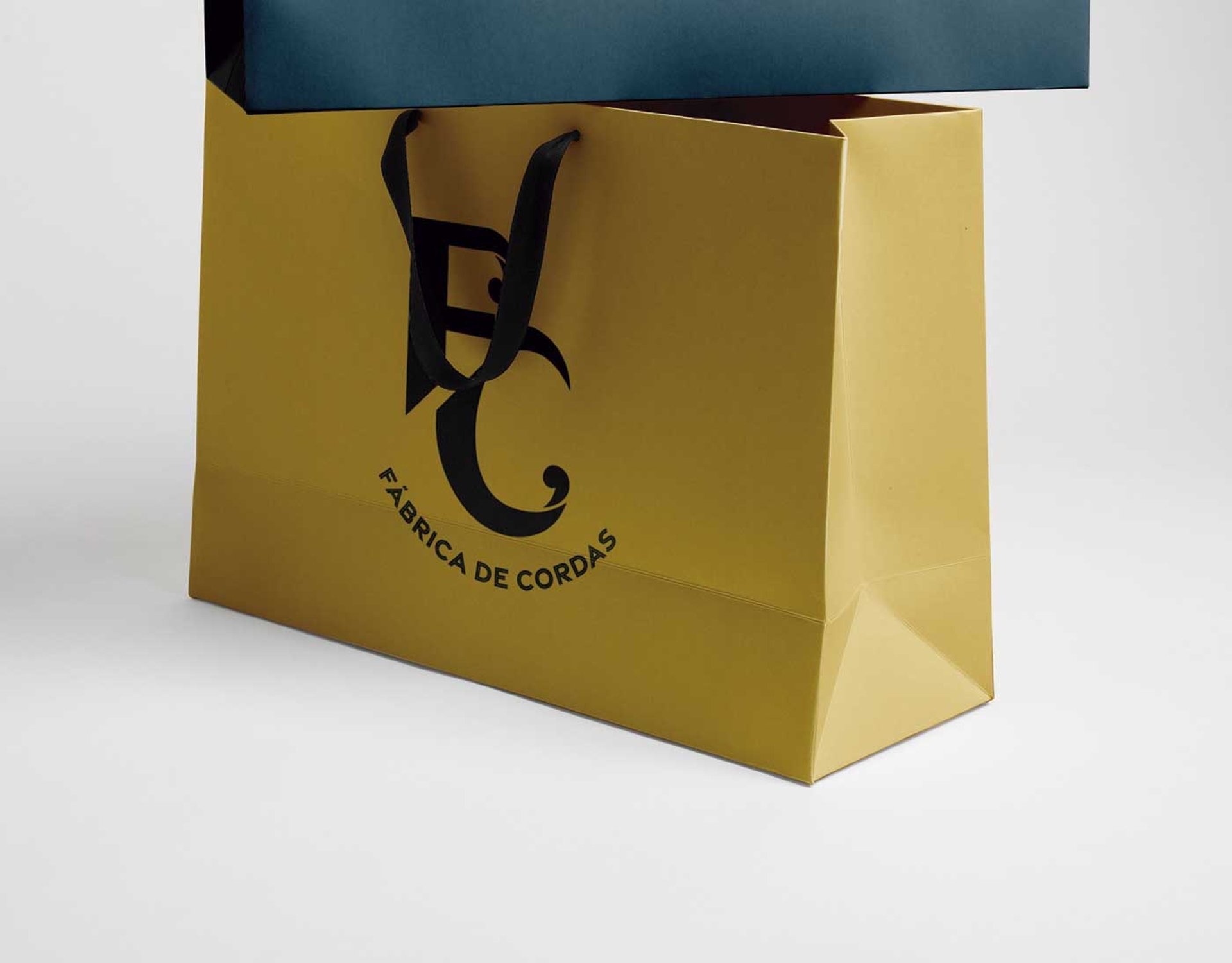 Mão segurando uma sacola com o logotipo da FC Fábrica de Cordas estampado, simbolizando compras e qualidade.