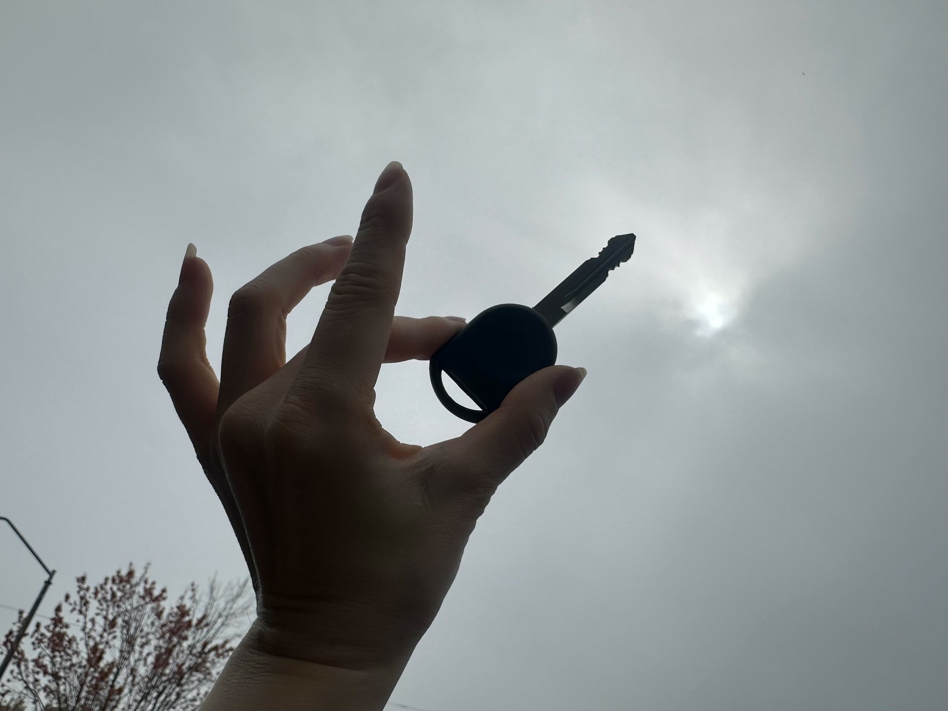 A hand holding a key silhouette against a cloudy sky