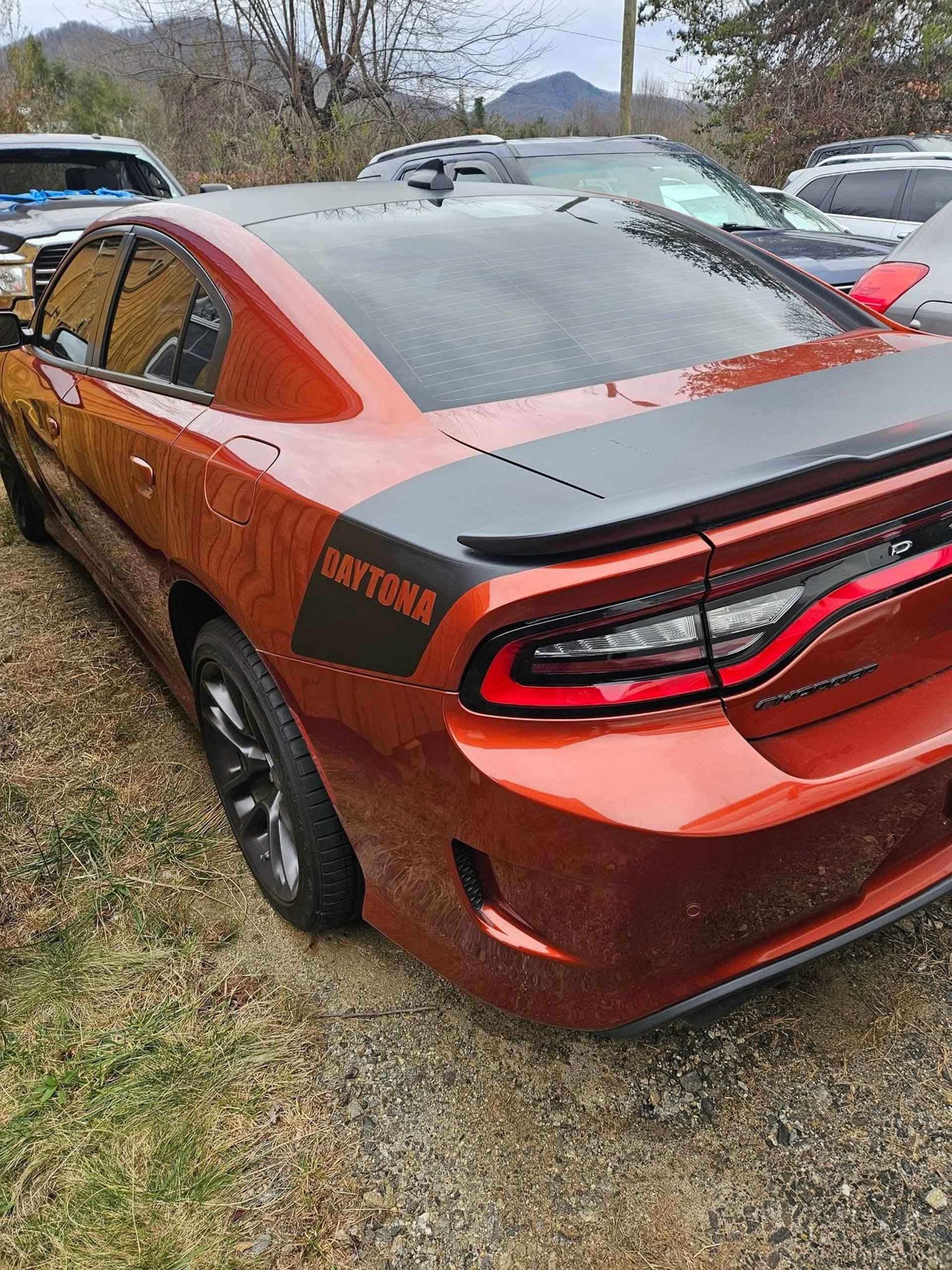 Orange Daytona Dodge Charger parked in a lot with mountains in the background