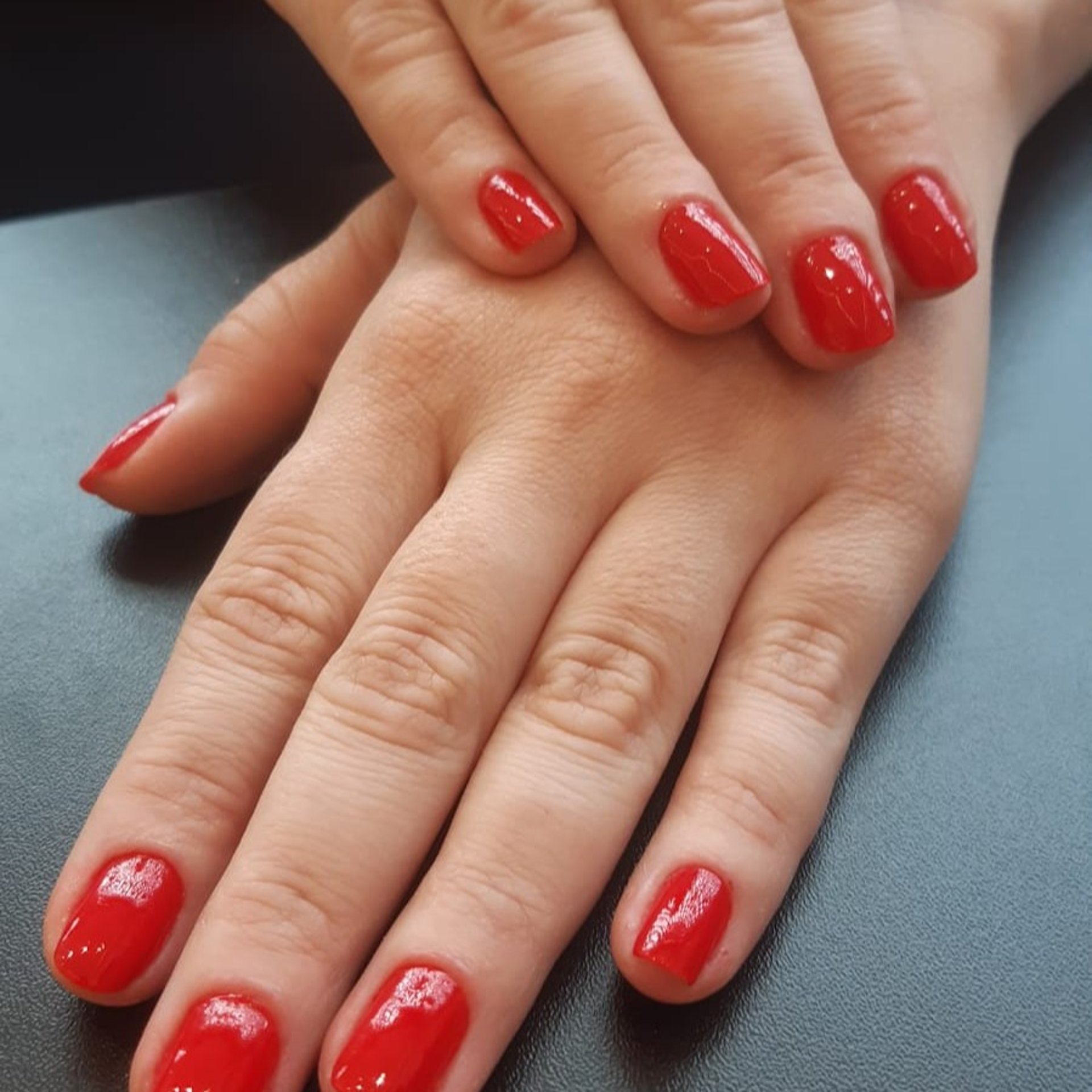 Detalhe de esmaltação vermelha em unhas quadradas, evidenciando a limpeza perfeita das cutículas e a qualidade dos materiais.