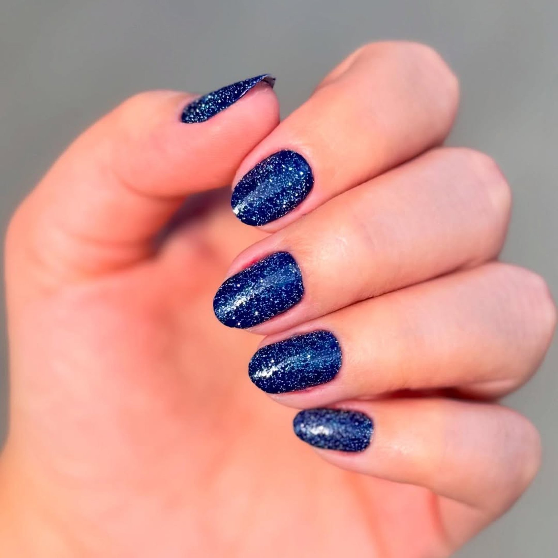 Esmaltação em gel azul marinho profundo com partículas de glitter prateado, apresentando brilho intenso e duradouro.