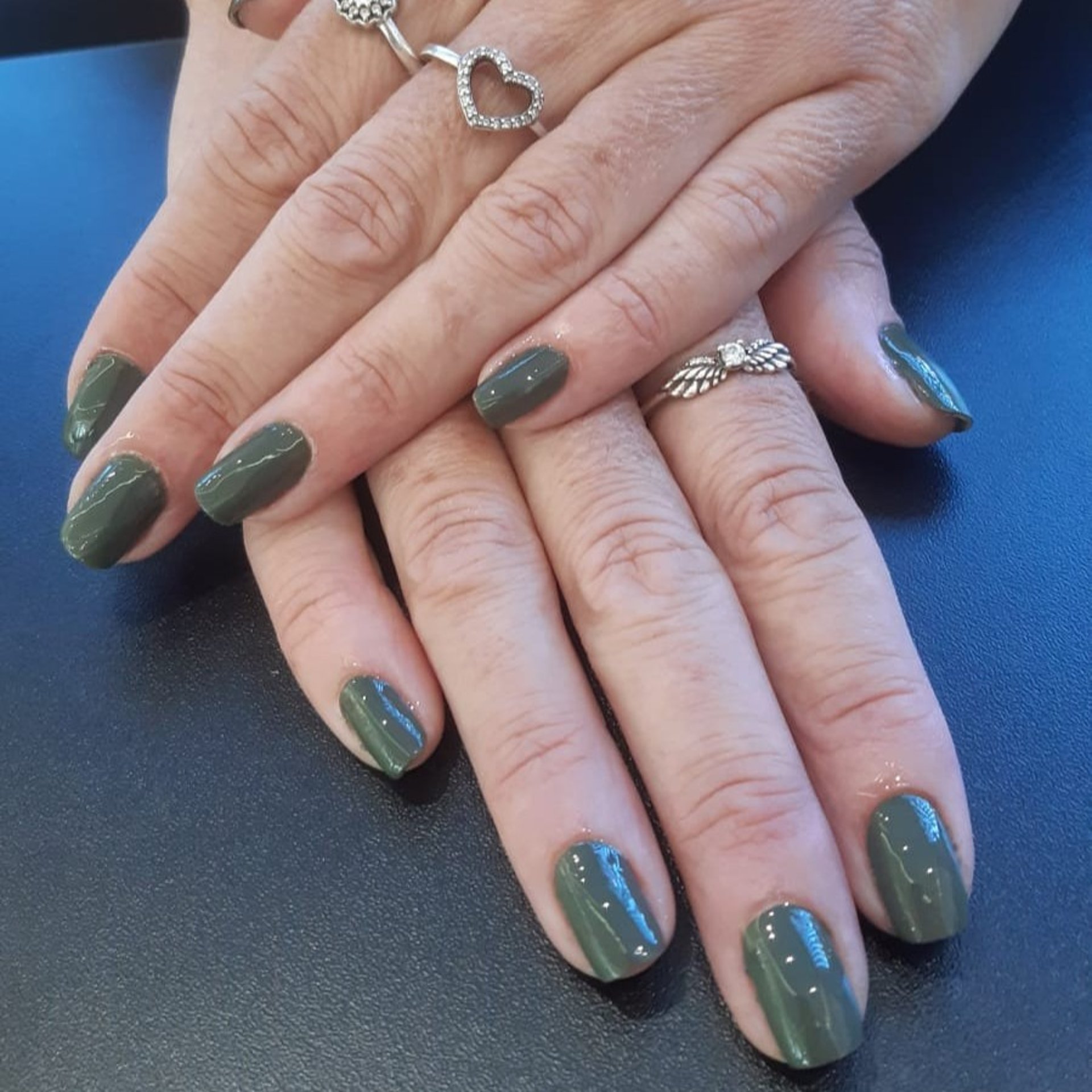 Unhas quadradas com esmalte verde militar cremoso, harmonizando com acessórios e demonstrando modernidade.