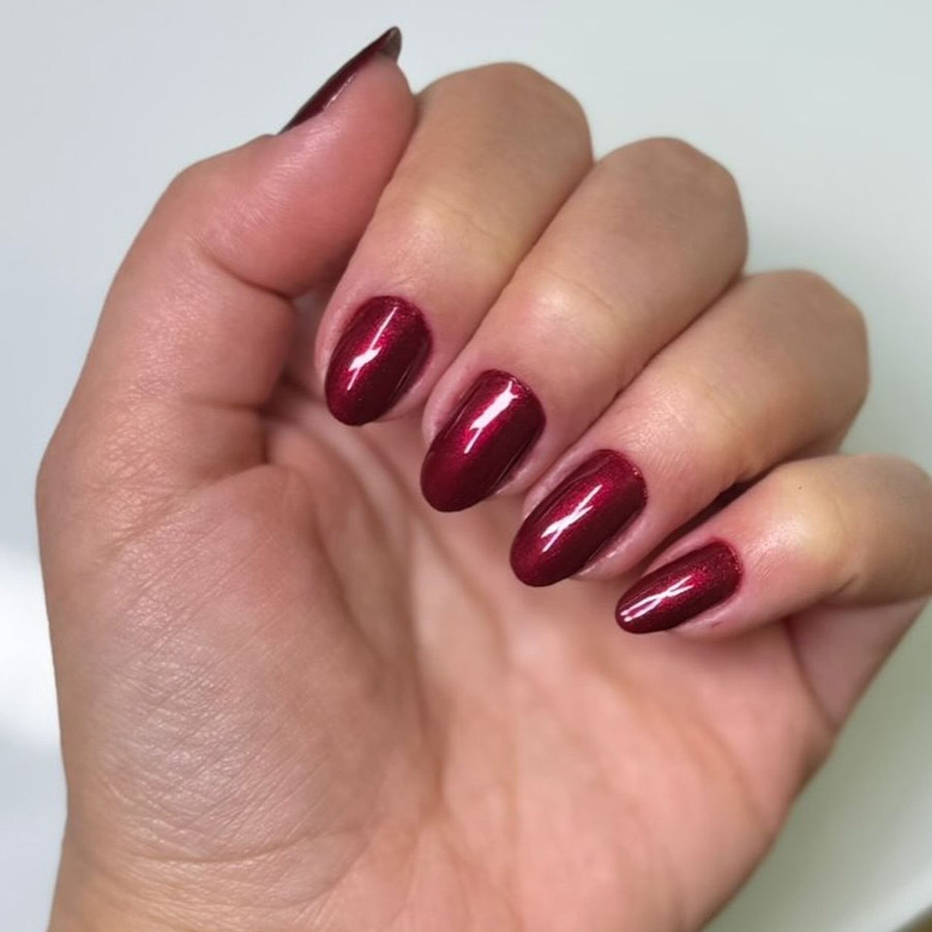 Manicure elegante com esmalte vinho metalizado em unhas ovais, focando na cobertura uniforme e no brilho espelhado.