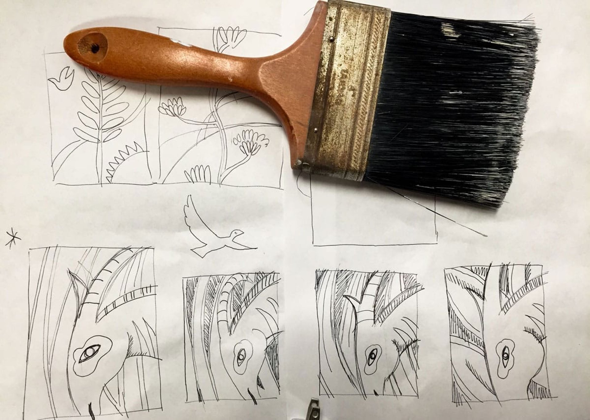 A broad painters' brush with black bristles lies on top of thumbnail sketches of Silver Antelope mural.