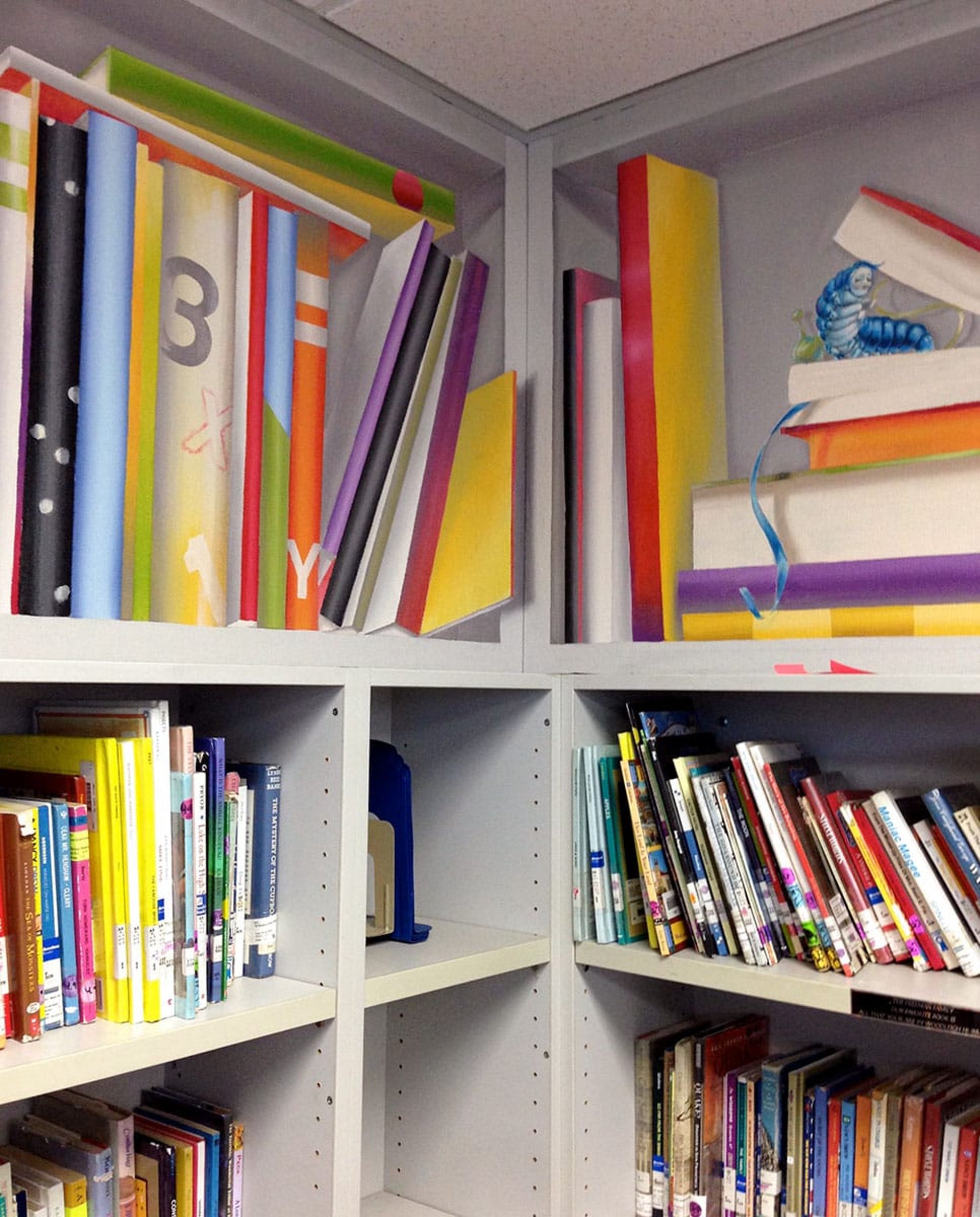 A corner of a kids' library adorned by a mural with colourful oversized books and a Caterpillar from Alice in Wonderland