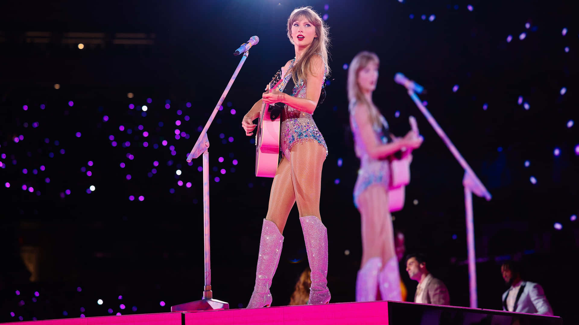 Taylor Swift playing guitar in glittering bodysuit and boots at Eras Tour show.