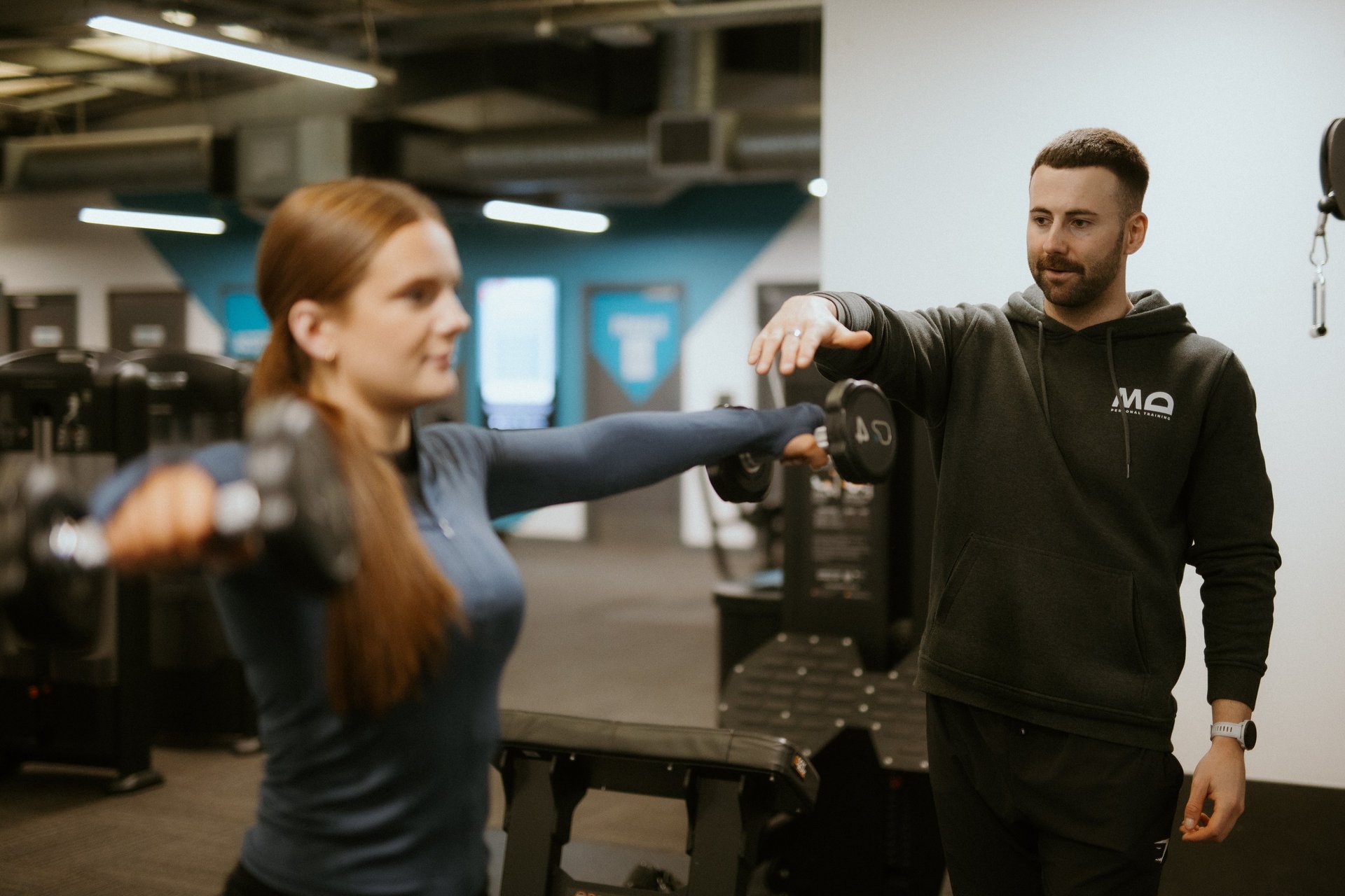 Client doing lateral dumbbell raise in Leamington Spa gym, coached by trainer focused on form and shoulder activation