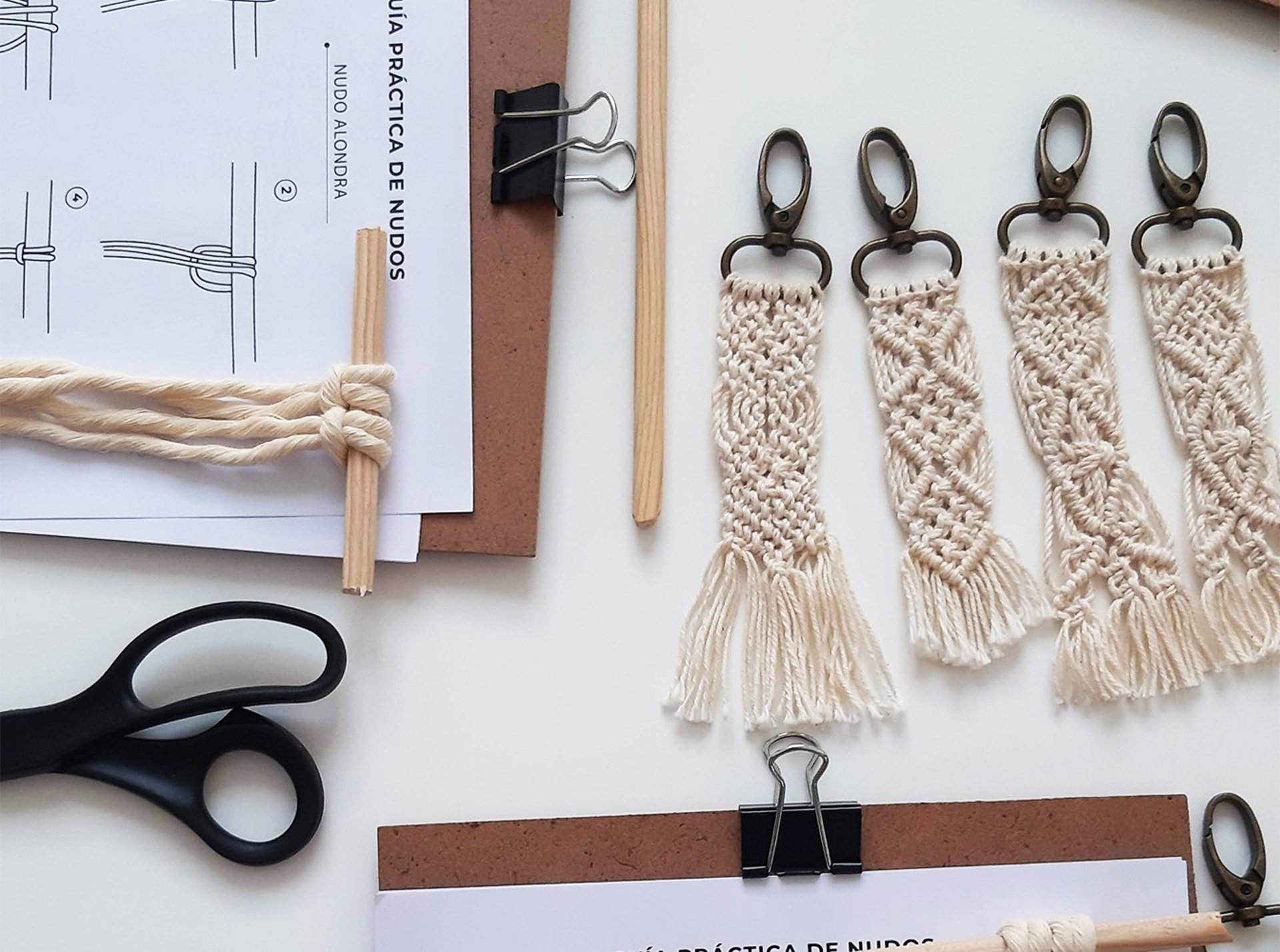 Llaveros de macramé sobre una mesa acompañados de material, tijeras e instructivos de nudos