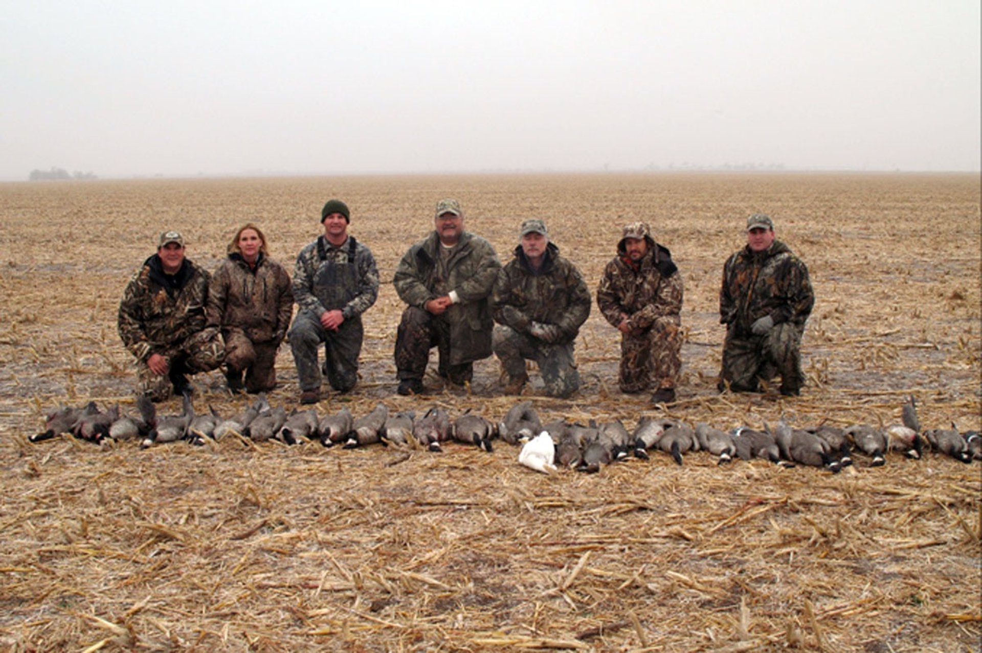 Five hunters in camo gear posing with their geese on a cloudy day in a Texas Panhandle field.