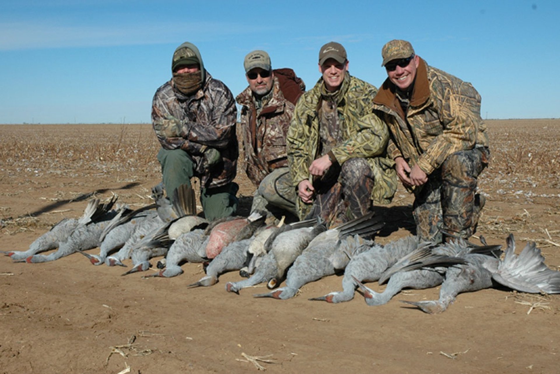 A group of hunters in camouflage with a black lab after a successful West Texas sandhill crane hunt.