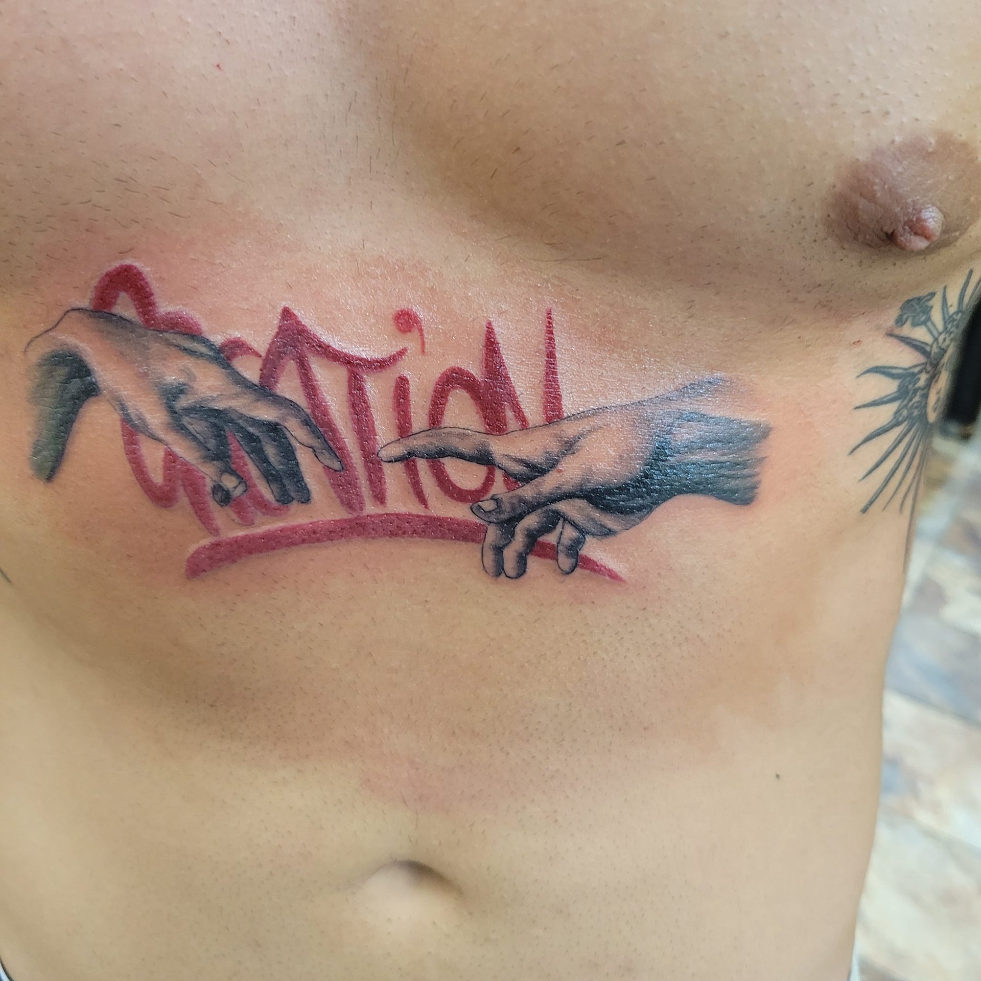 Tatuaje de la creacion de Adan en black and grey con un fondo de lettering estilo graffiti en tinta roja Leon Guanajuato 