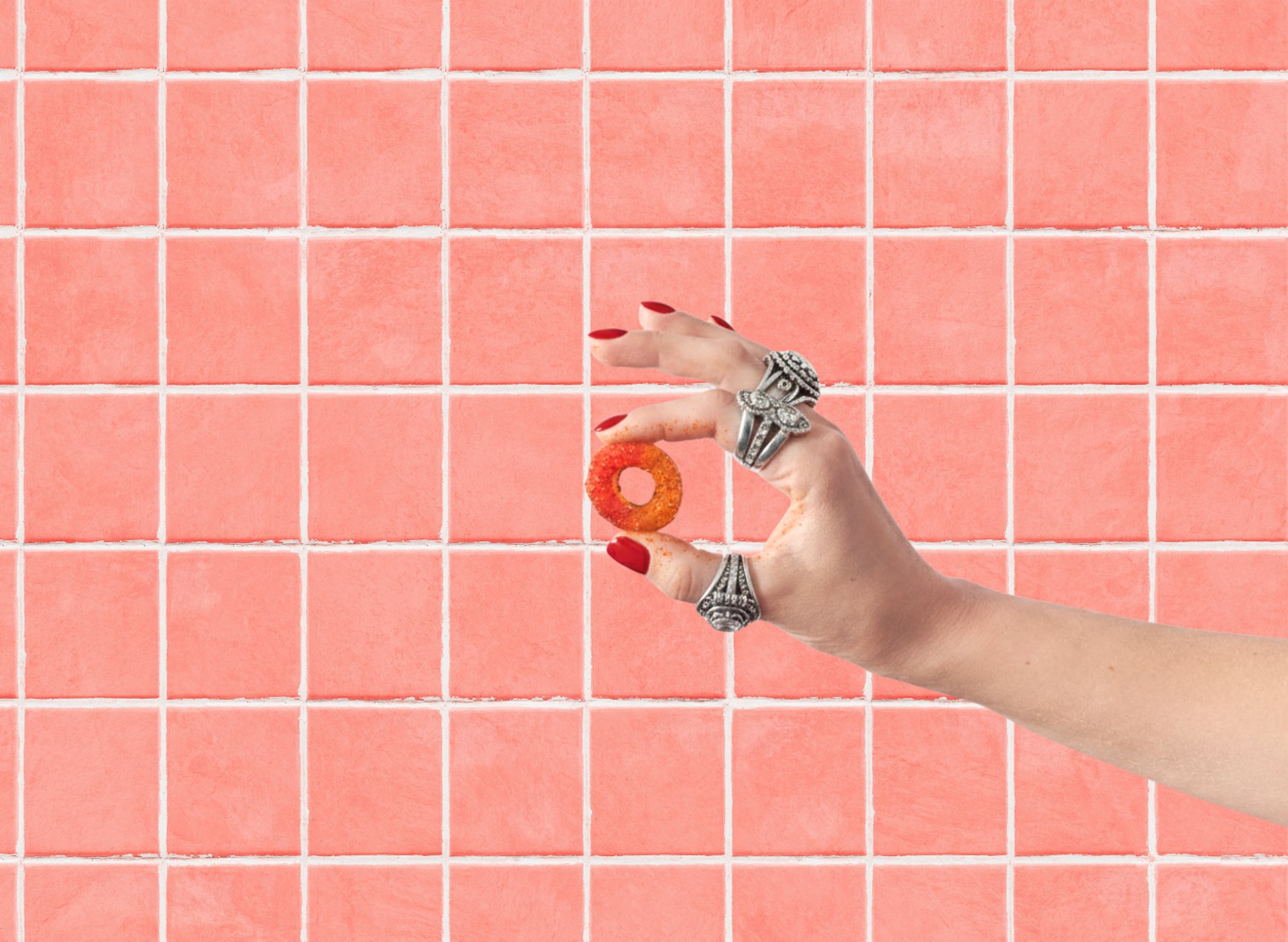 pink tiles background showing a hand with silver rings holding a chili gummy