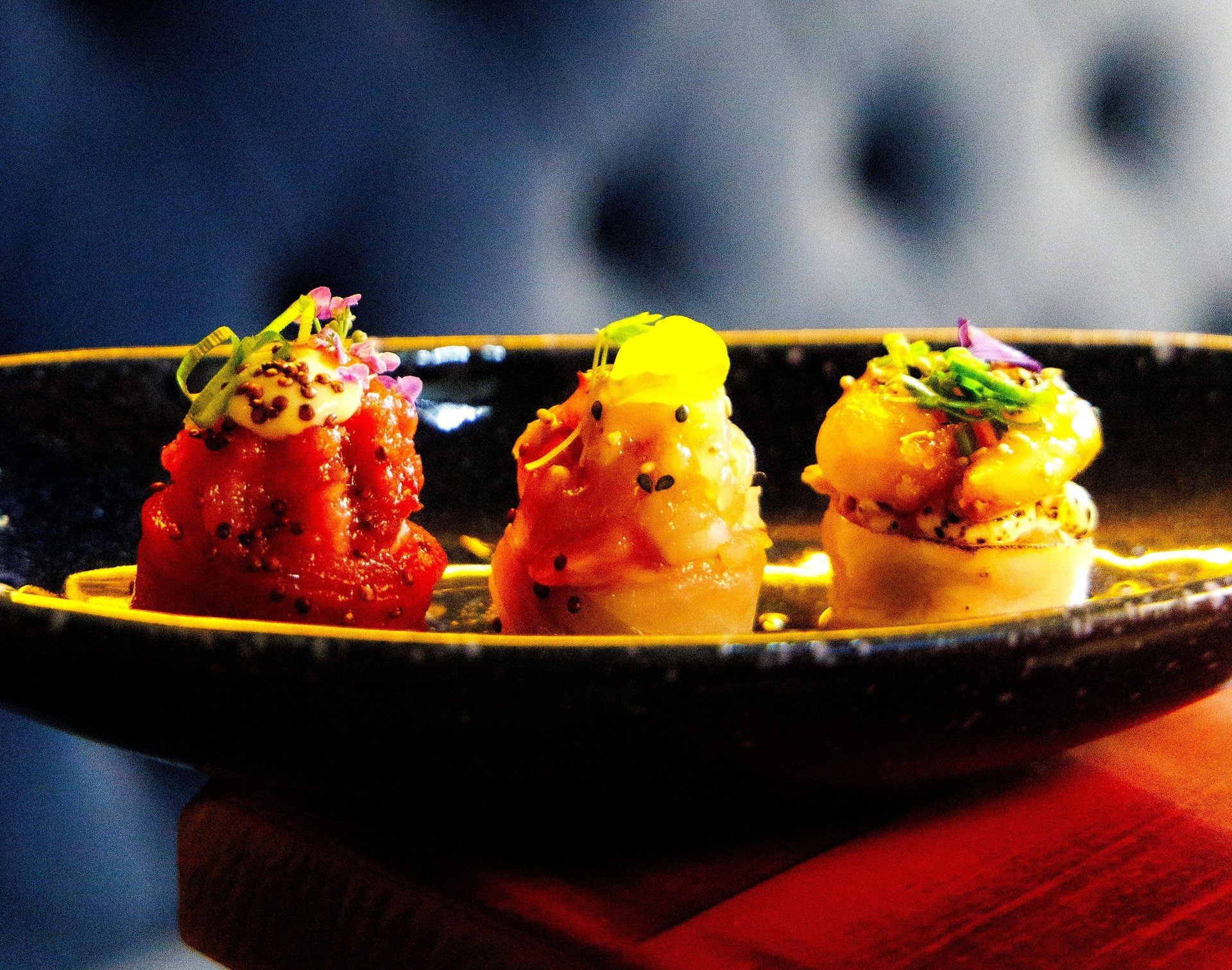 Close de três peças de sushi autoral decoradas com flores e ovas, servidas em um prato fundo no Okone Porto