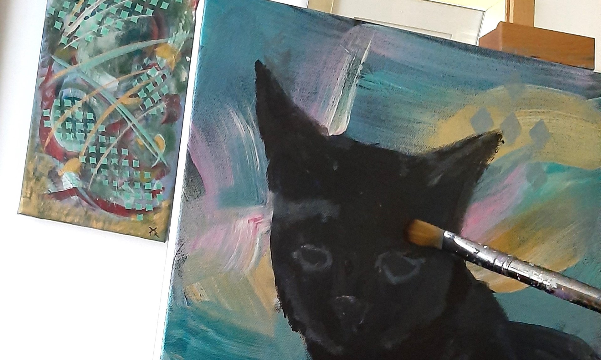 My paintbrush working on a canvas of a black cat, with one of my old abstracts to the left.
