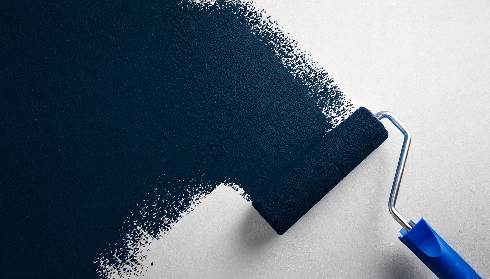 Paint roller applying navy blue paint over a white wall, showing the transition mid-stroke