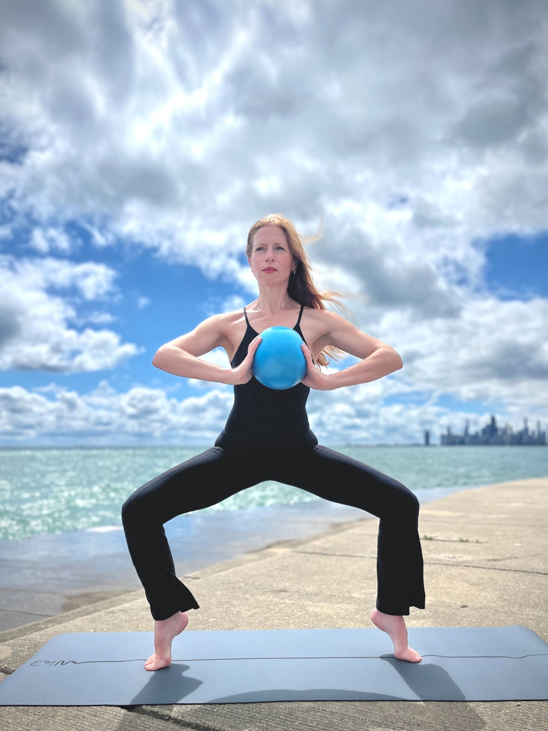 Kathryn Norris outdoors in saddle pose, surrounded by greenery, embodying mindfulness and a deep connection to nature.