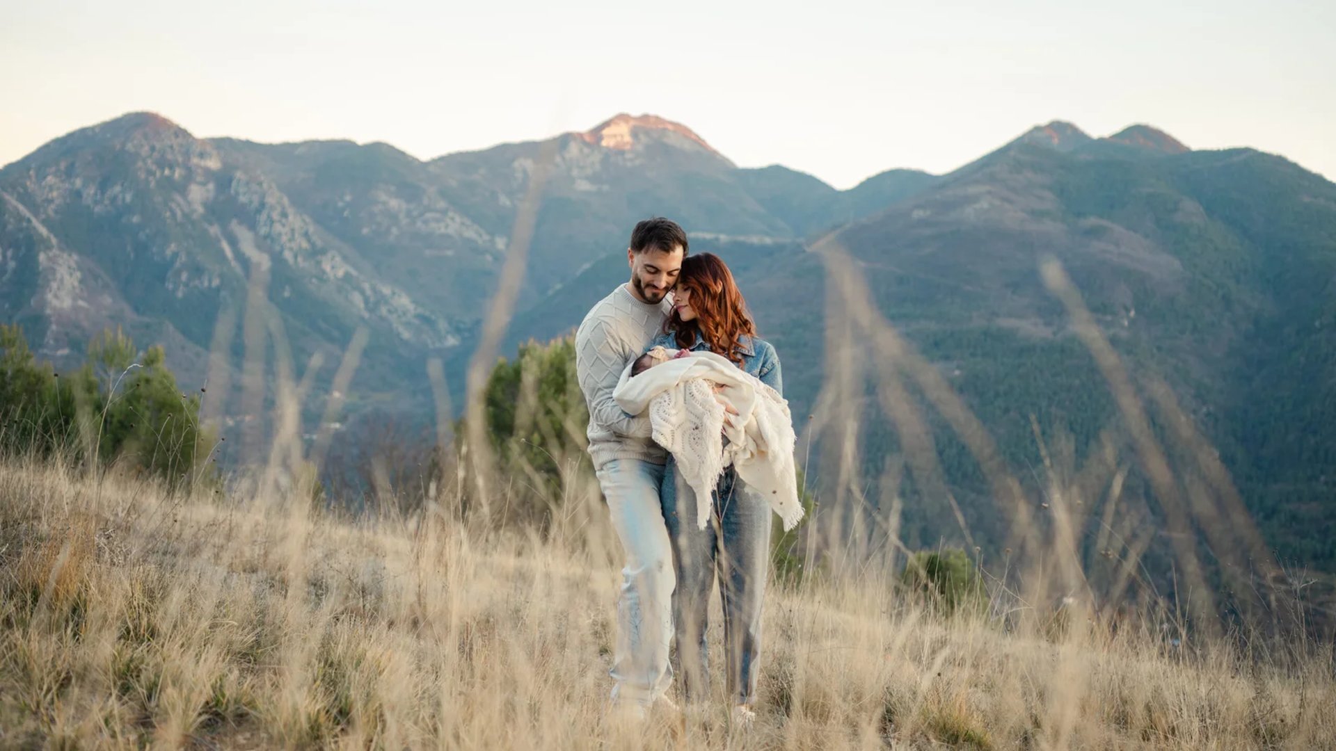 séance photo nouveau né, un couple tenant un enfant, sur une vue montagne, par le studio des 4 saisons