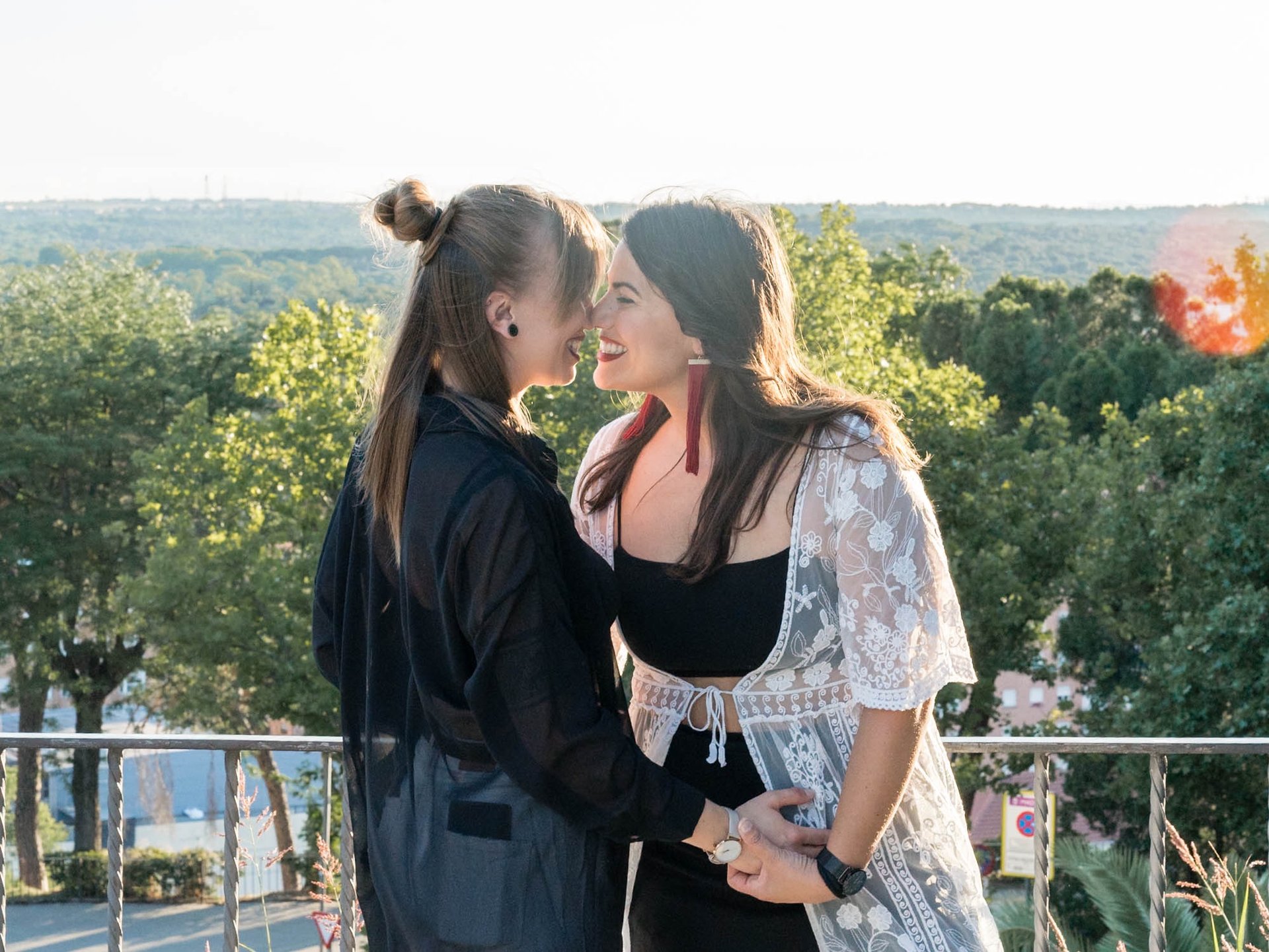 "Pareja lesbiana sonriendo y tocándose suavemente en Madrid, celebrando su amor y su relación."