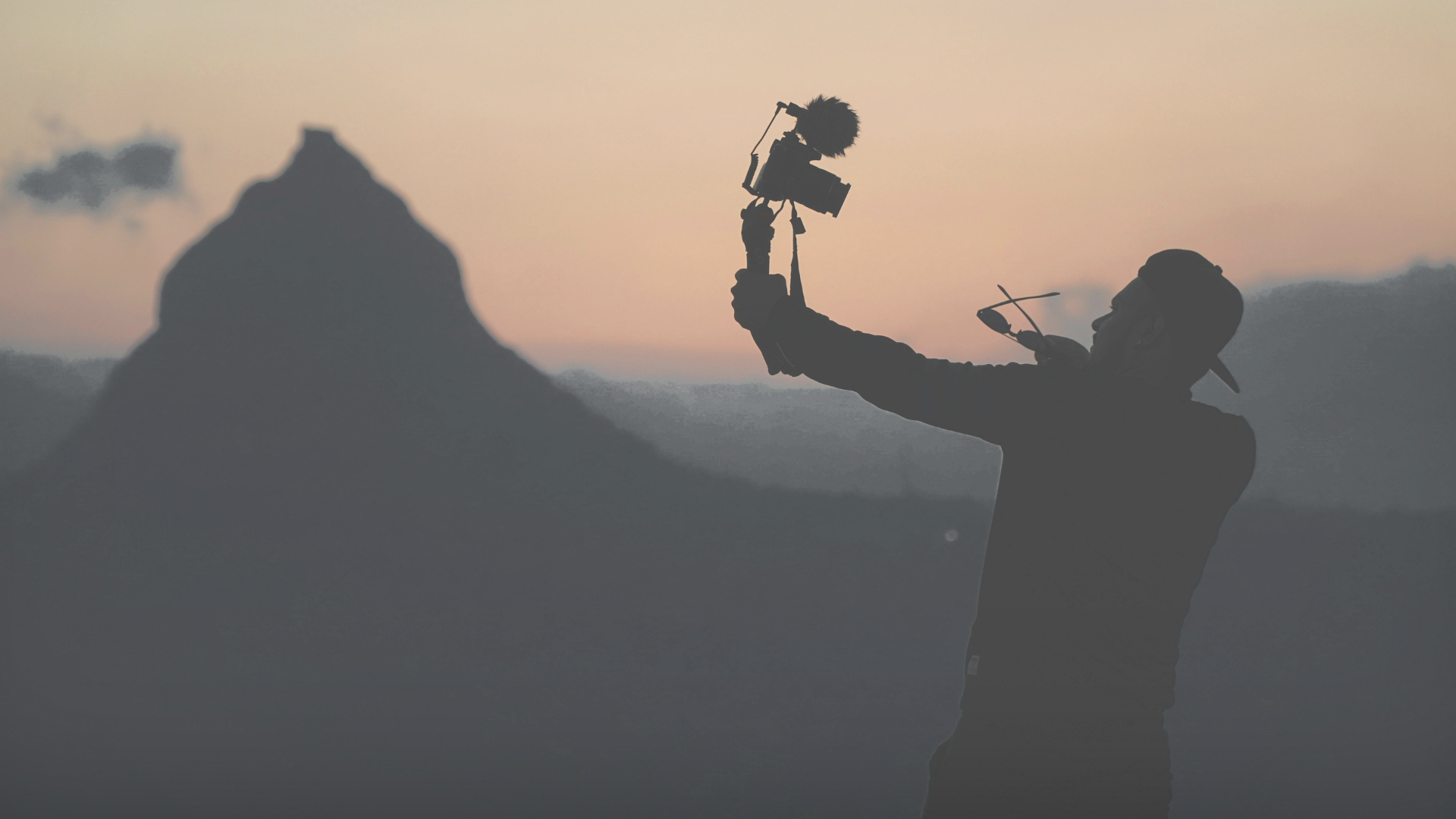 silhouette of man standing beside camera tripod during sunset