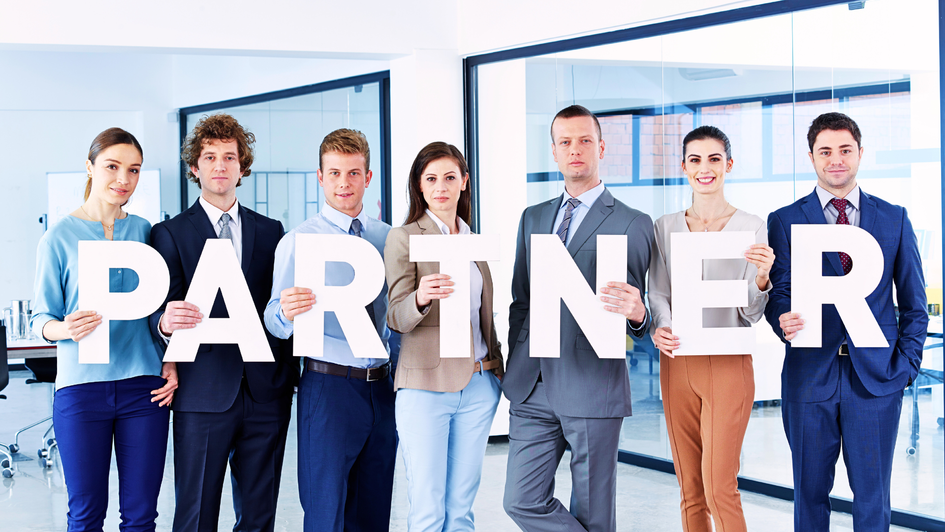 Group of business leaders in suits stands in a line, each holding up a letter to spell out the word "Partner" in the office.