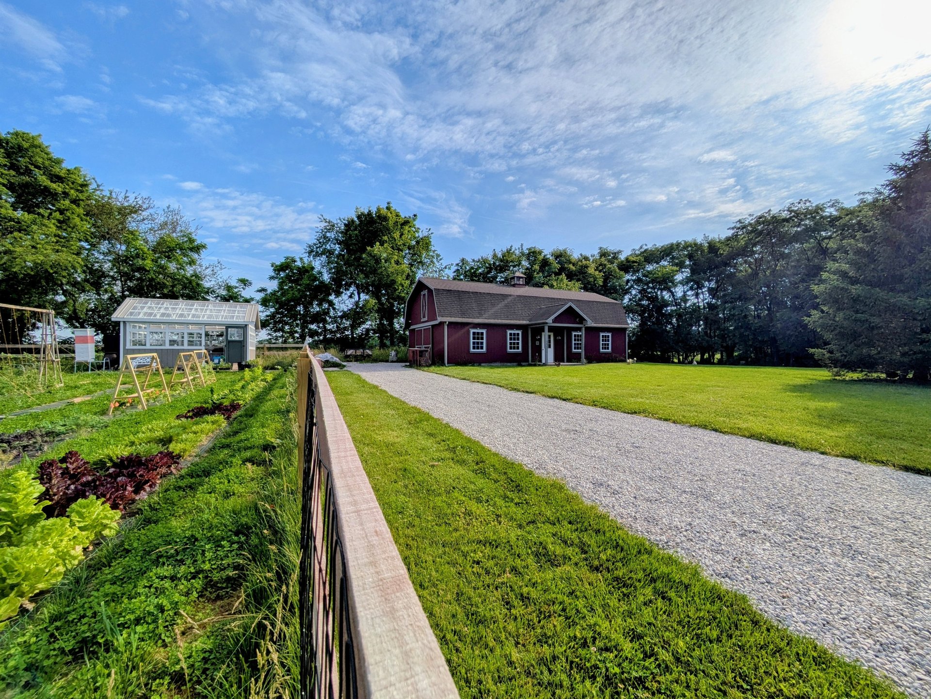 A sunny image of a barn, greenhouse, and garden