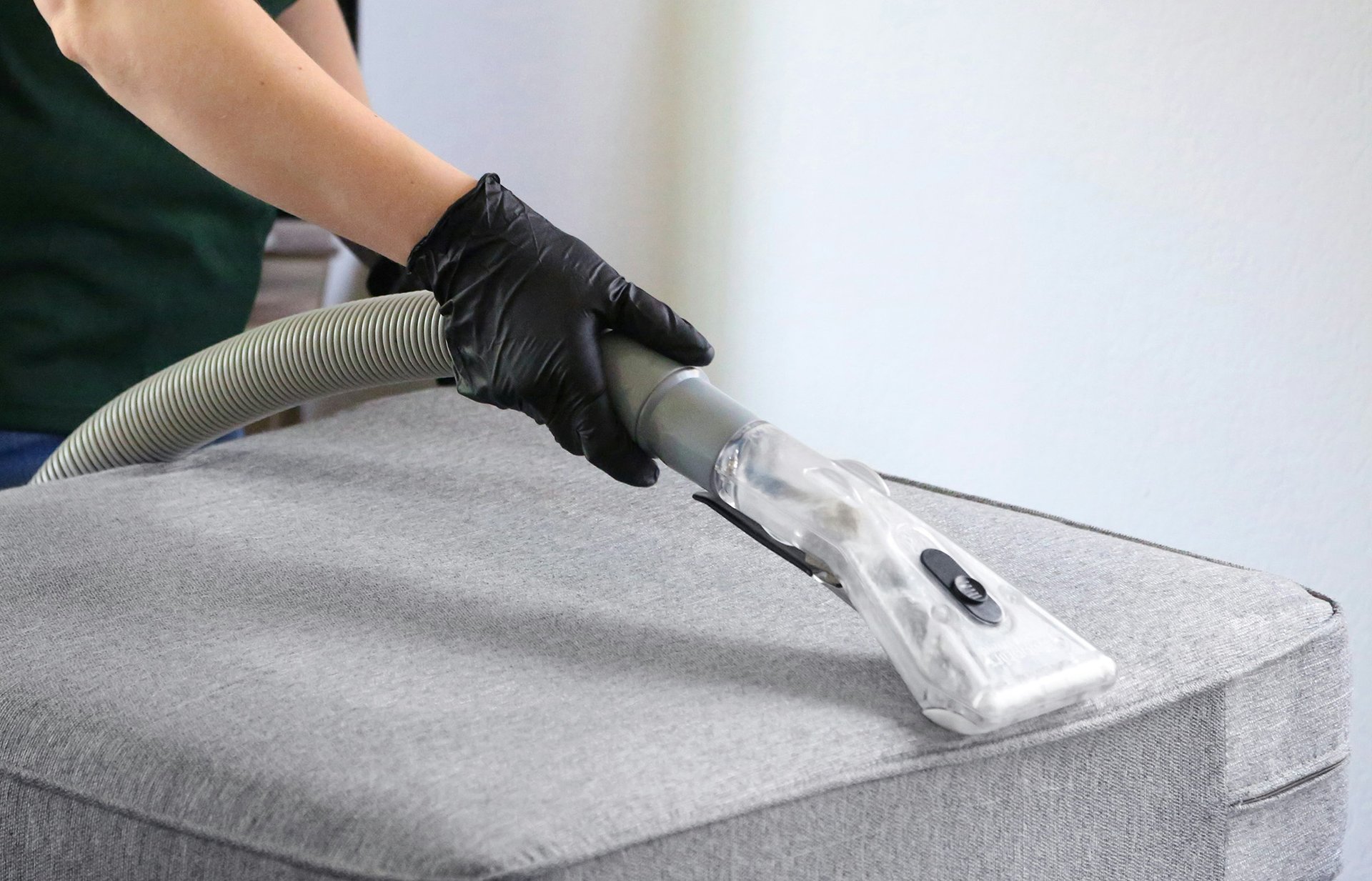 a woman in a green shirt and black gloves vacuuming a gray ottoman