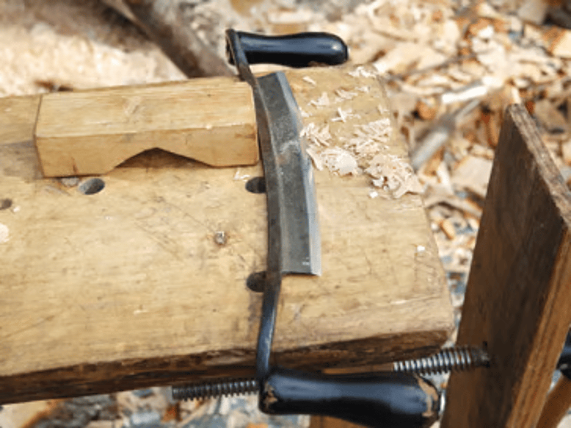 image shows a board piece of timber and curved drawknife 